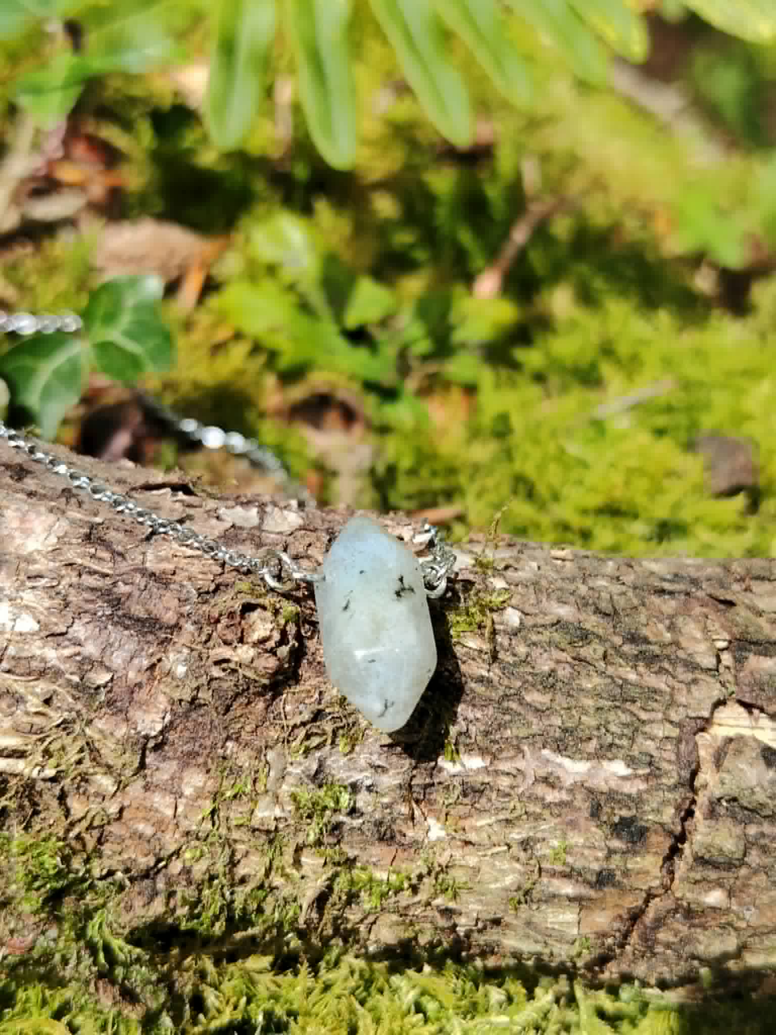 Pendentif pointe Labradorite sur bois moussu en forêt, pierre naturelle claire avec inclusions sombres, chaîne acier inoxydable argentée.