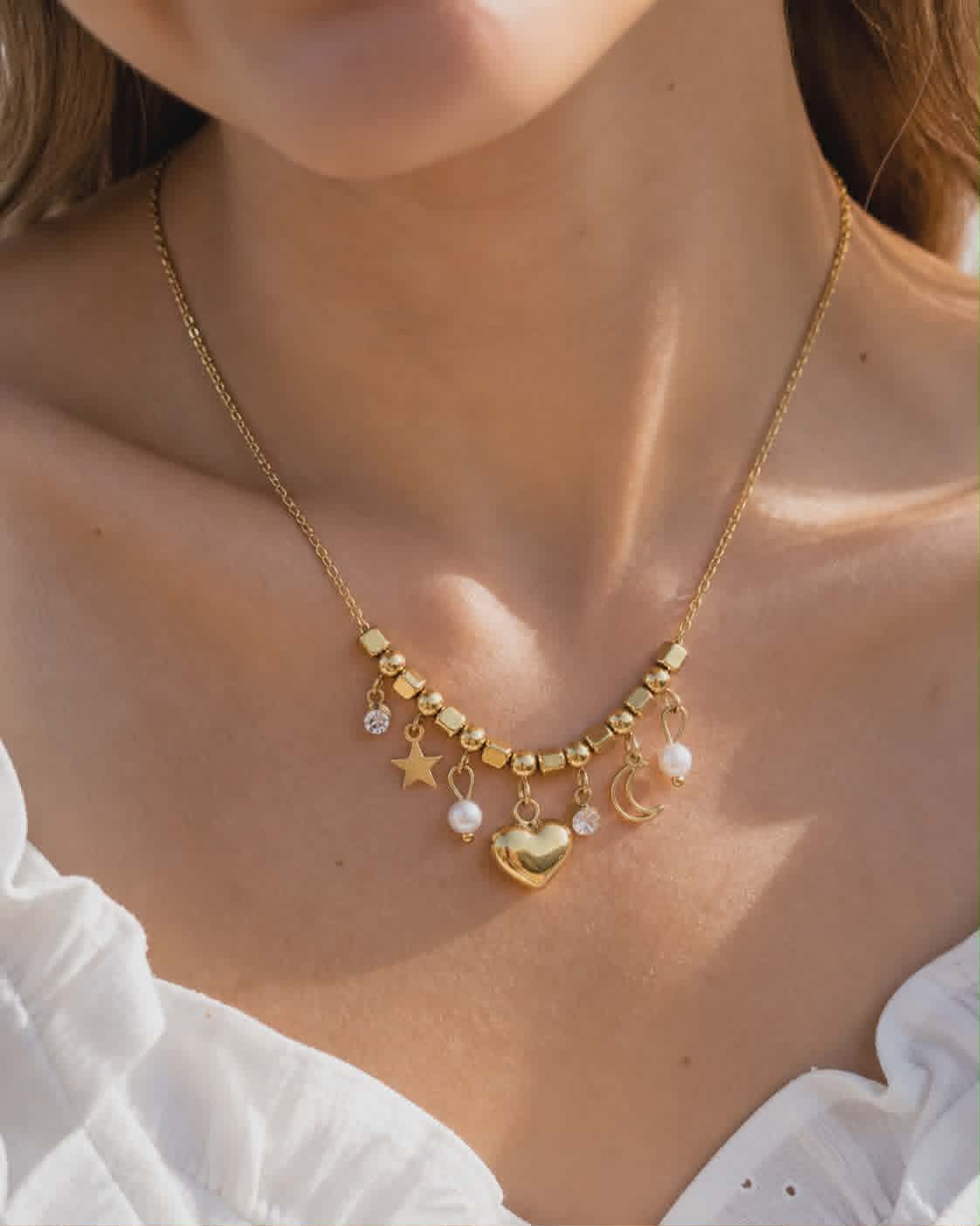 Collier doré cœur lune étoile porté au cou avec haut blanc, perles décoratives et pendentifs fins pour un style céleste élégant.