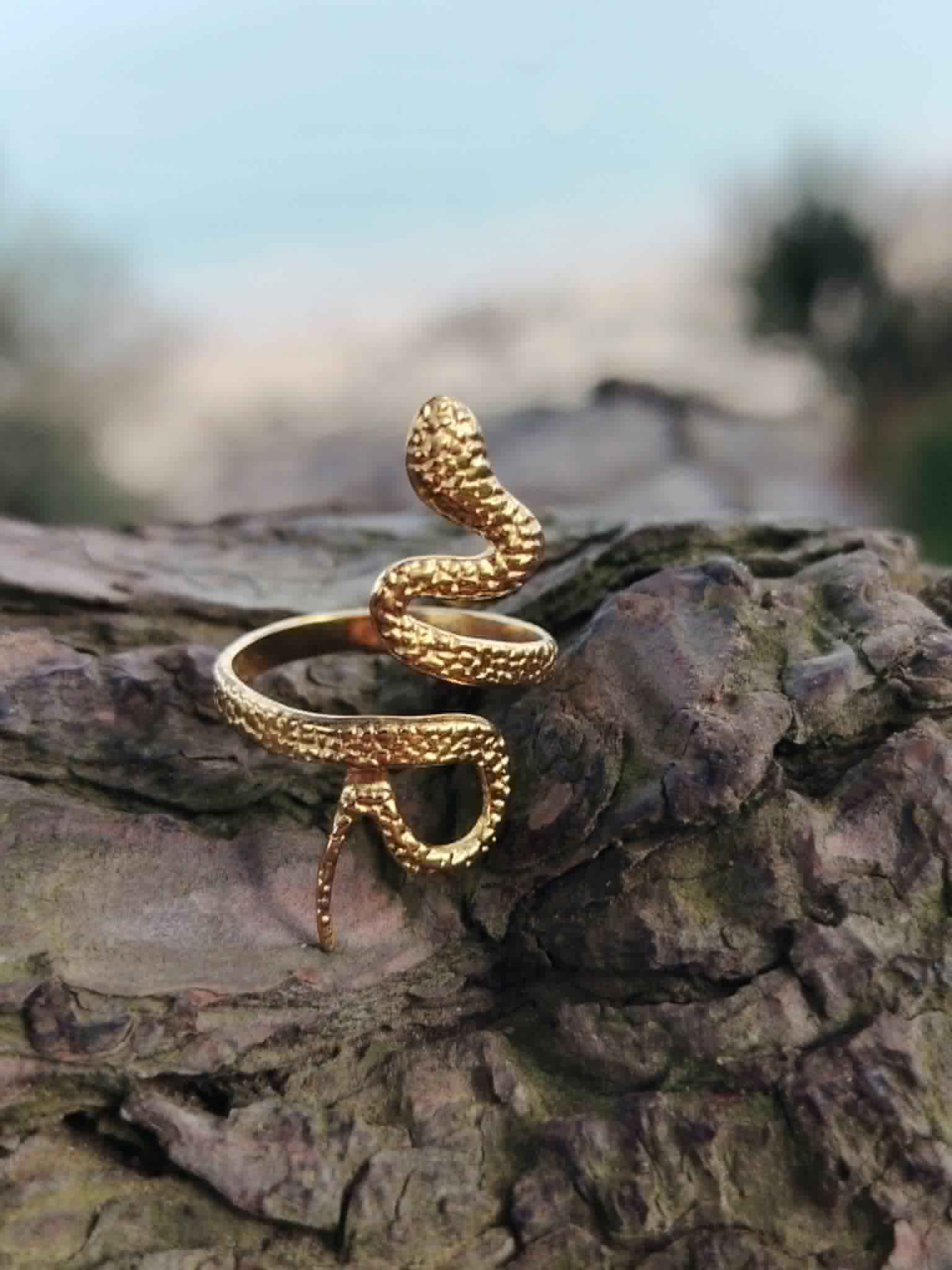 Bague serpent dorée ajustable en acier inoxydable posée sur écorce, bijou symbolique pour transformation, instinct et renouveau.