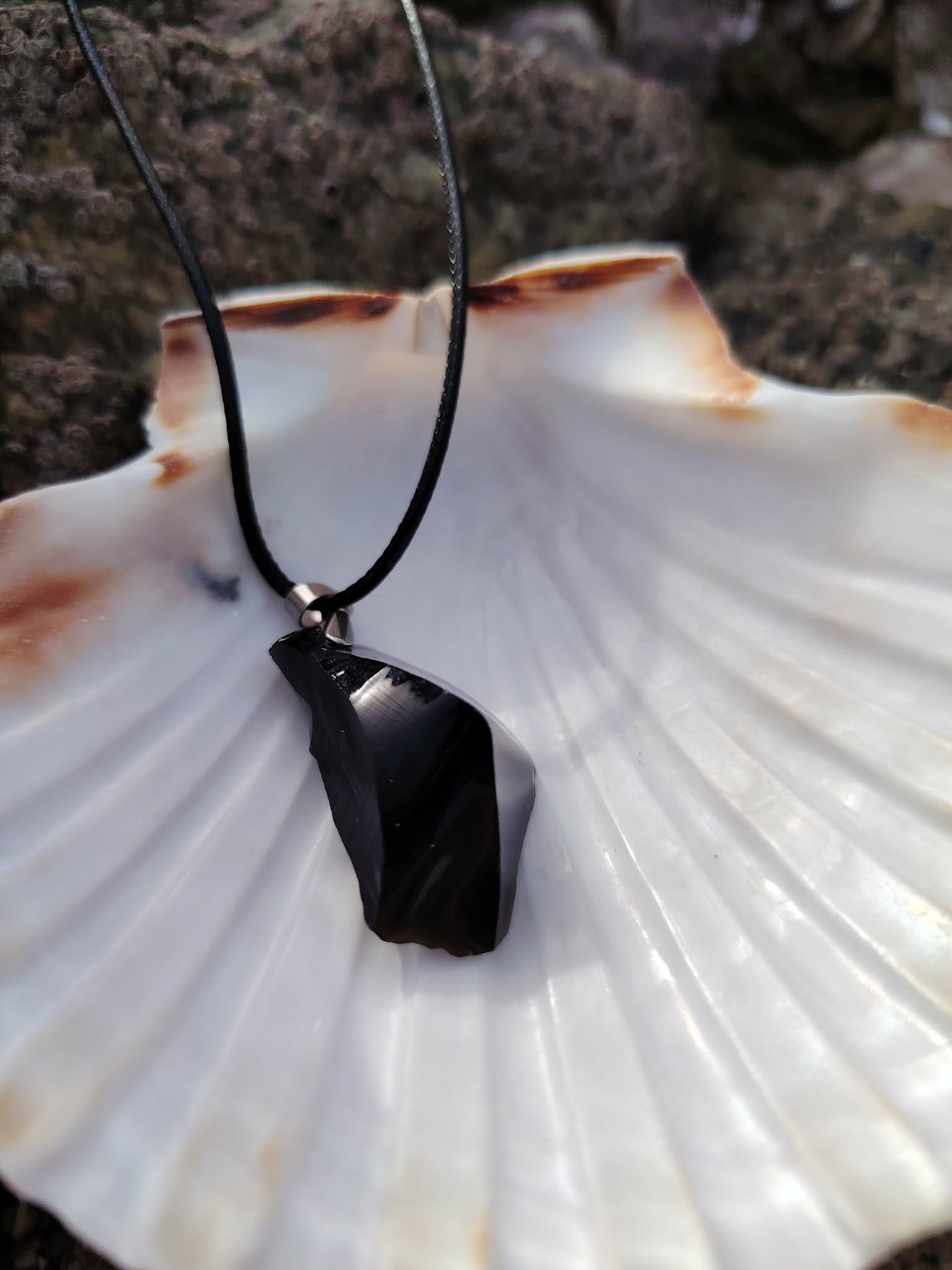 Obsidienne noire repolie en pendentif sur coquille Saint-Jacques, cordon noir et éclat vitreux pour ancrage symbolique.