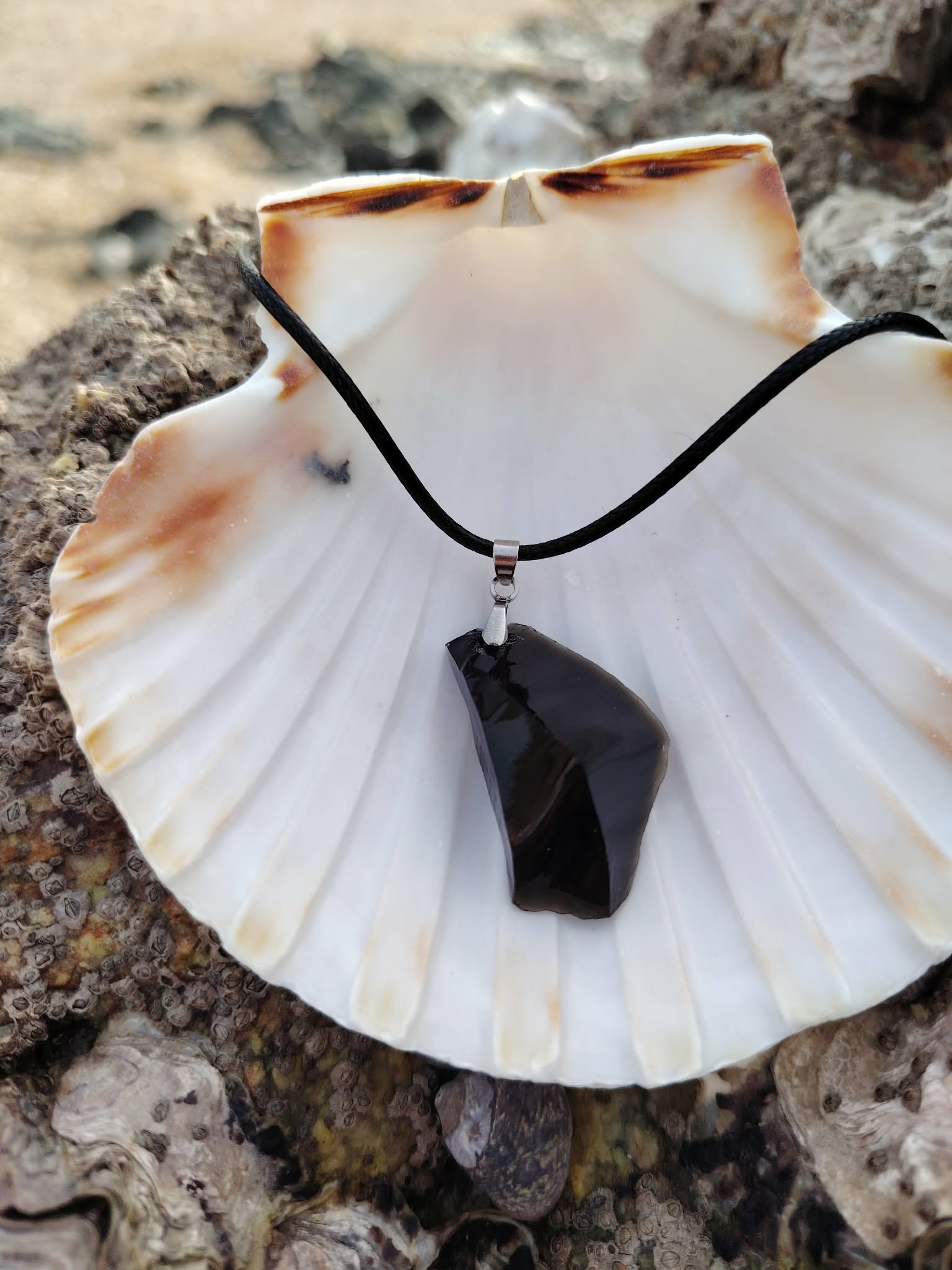 Pendentif Obsidienne noire création Magic Gaïa sur coquille et rochers bretons, pierre percée repolie au noir volcanique.