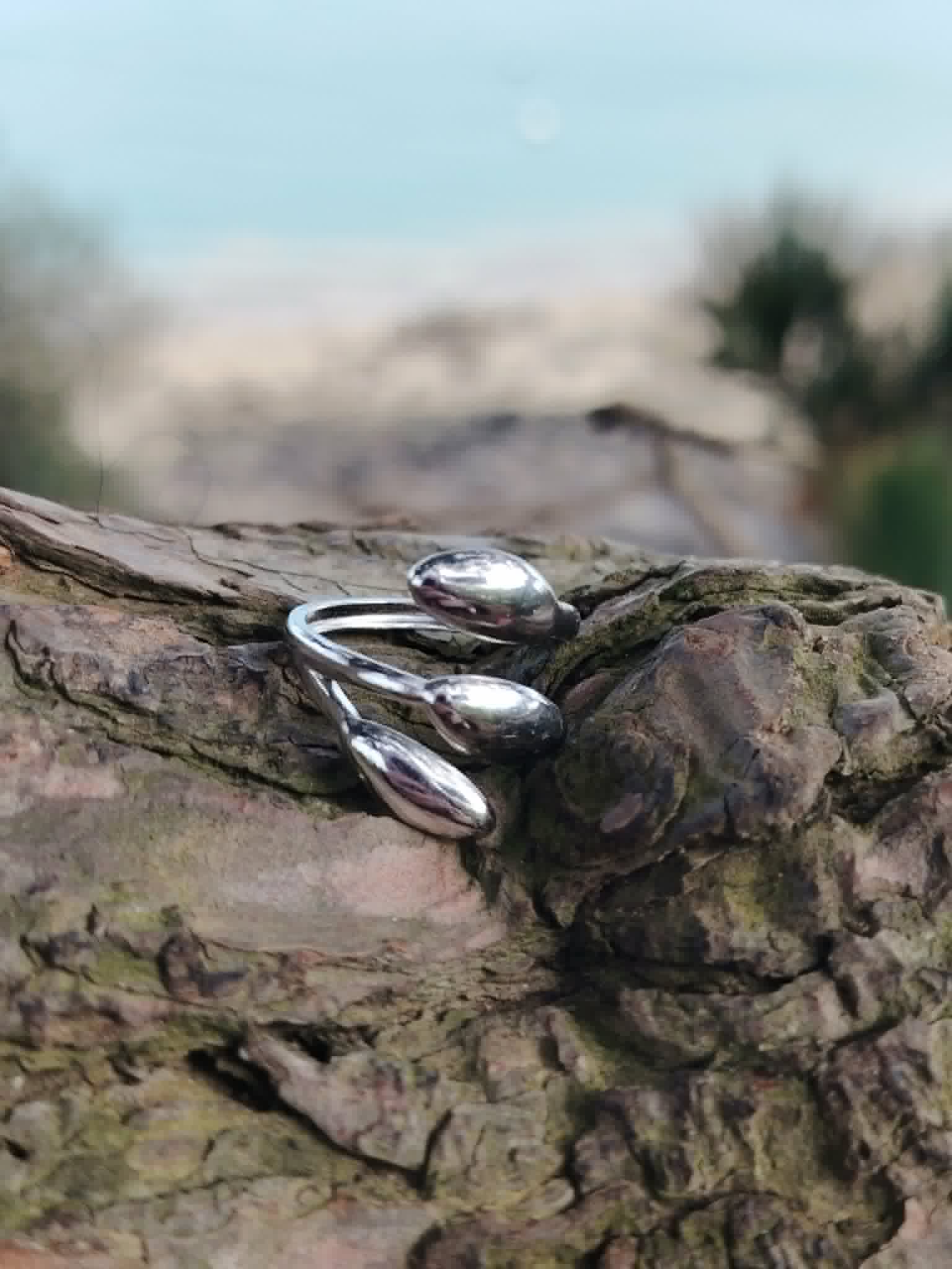 Bague argentée ajustable triple goutte en acier inoxydable sur écorce, bijou brillant au design moderne et sculptural.