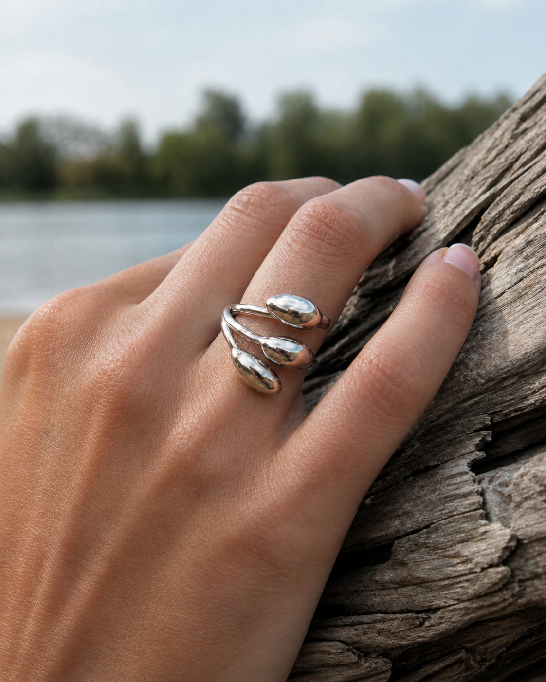 Bague argentée triple goutte portée au doigt près du bois, bijou ajustable lumineux au style fluide et élégant.