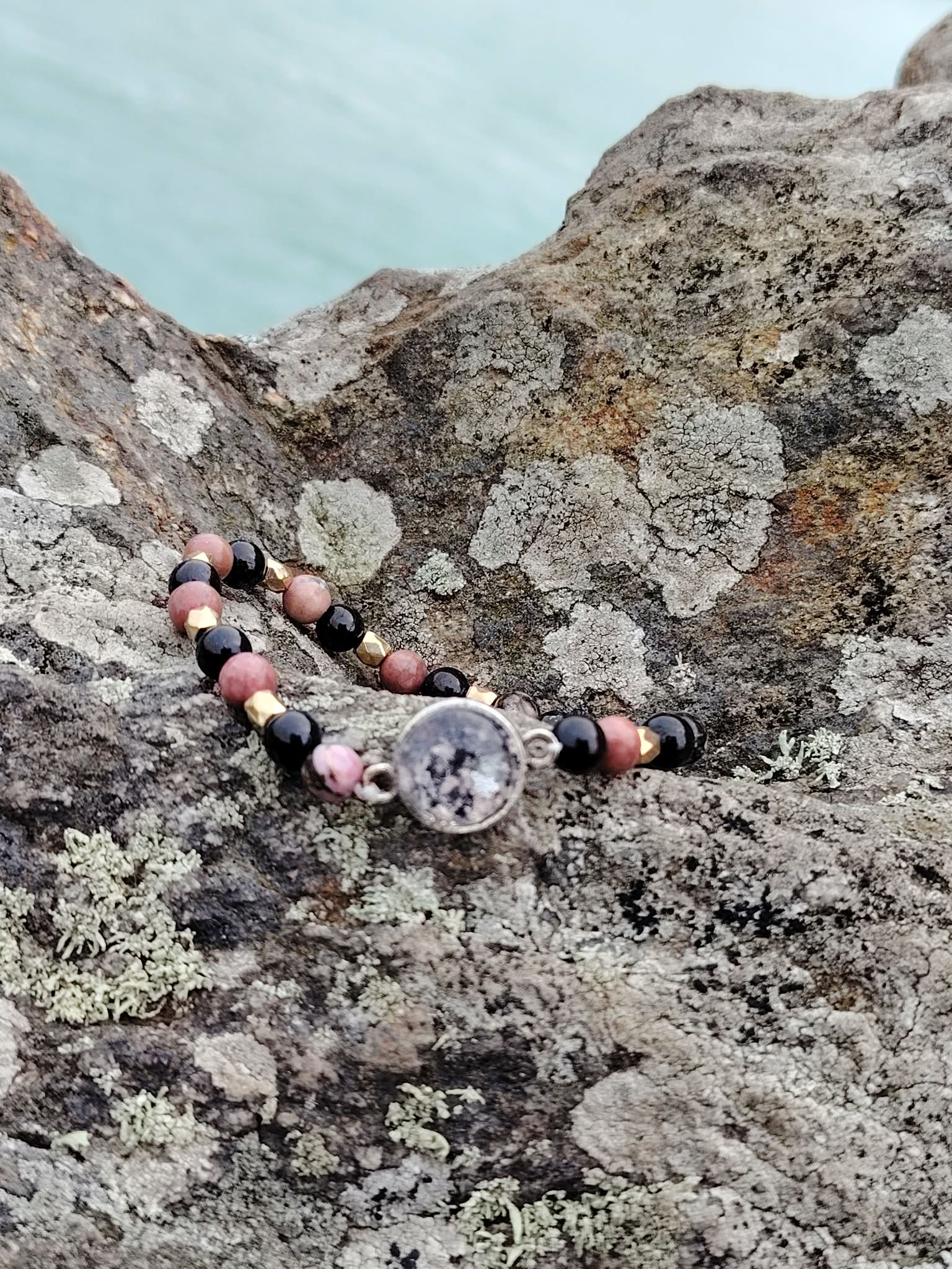Gros plan sur bracelet Rhodonite Tourmaline Noire, perles naturelles roses et noires, détails dorés et cabochon argenté.