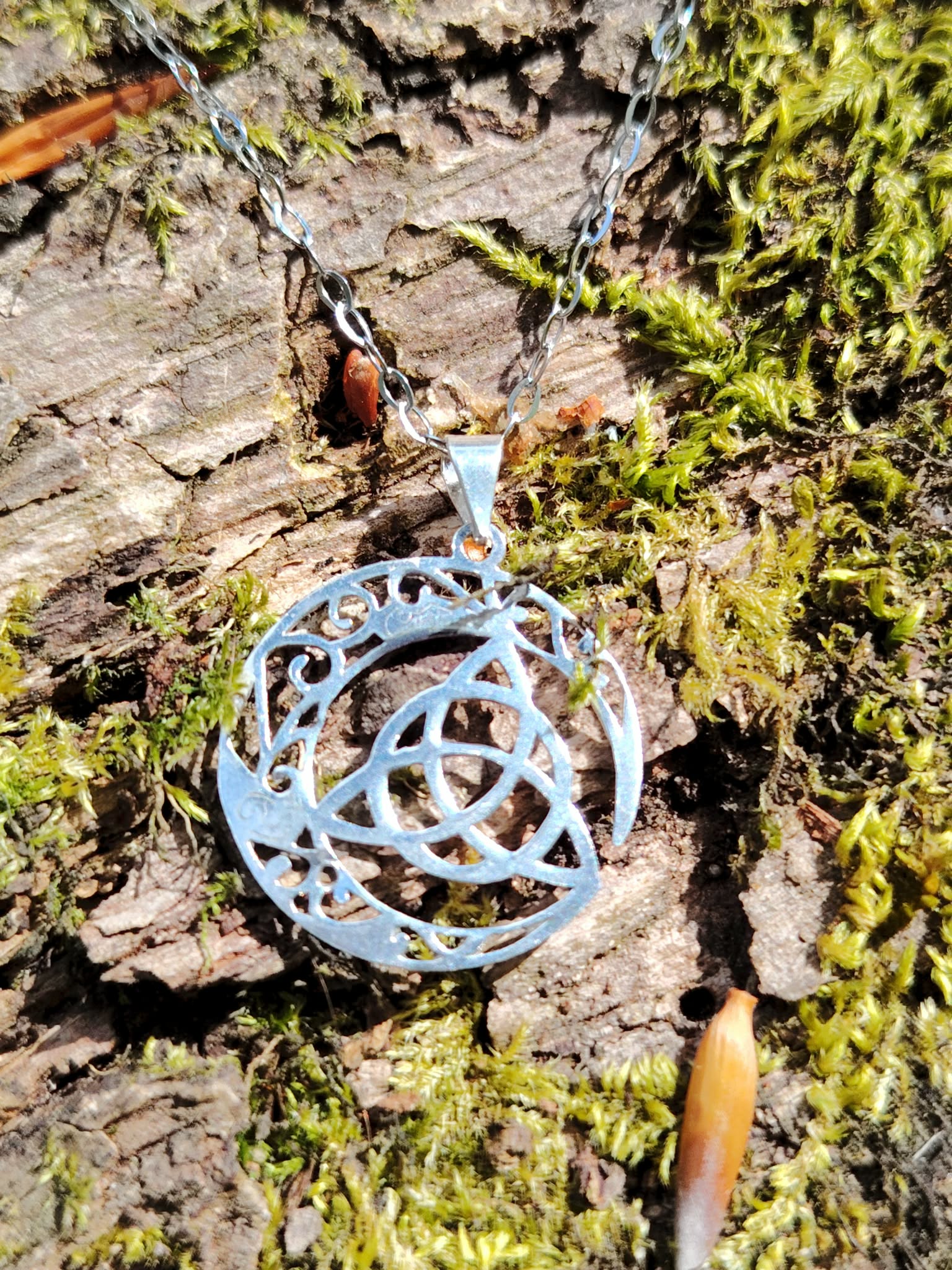 Pendentif Triquetra Lune argent 925 sur écorce et mousse, symbole celtique ajouré avec croissant lunaire.