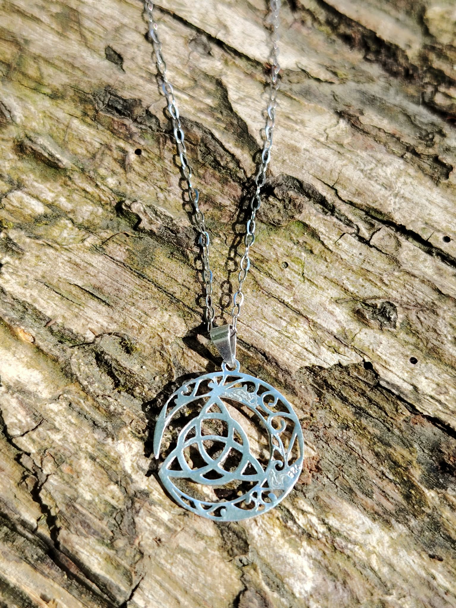 Pendentif Triquetra Lune argent 925 sur écorce, chaîne argentée et motif celtique ajouré en croissant.