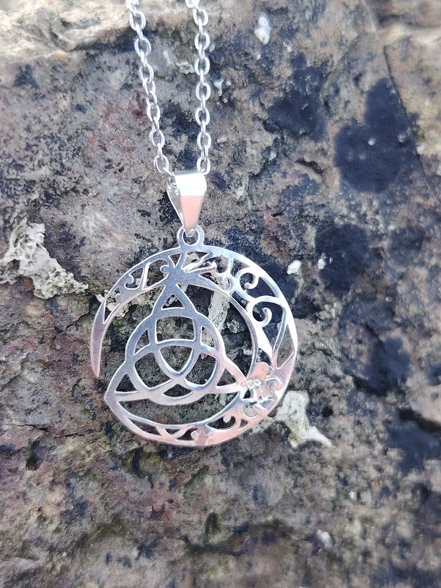 Pendentif Triquetra Lune argent 925 posé sur roche naturelle, motif ajouré celtique aux reflets argentés.