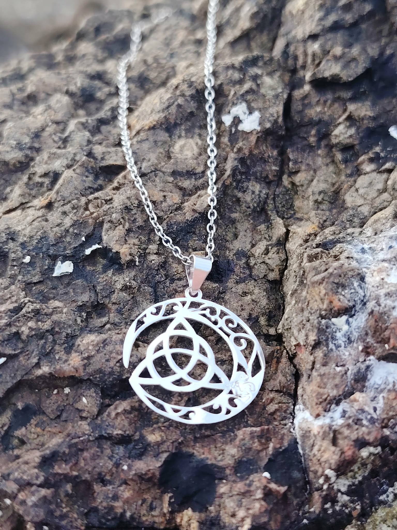 Gros plan sur pendentif Triquetra Lune argent 925 posé sur roche, croissant ajouré et chaîne argentée.