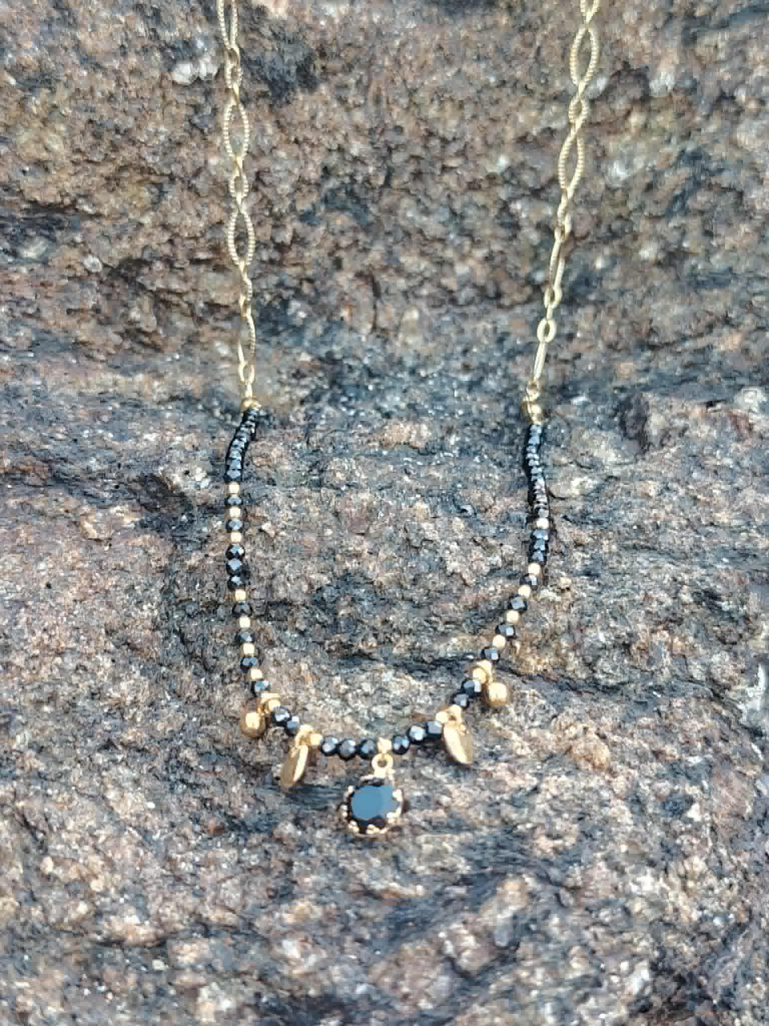 Collier doré Onyx pierres naturelles sur décor clair, détails noirs et dorés pour un rendu élégant, profond et raffiné.