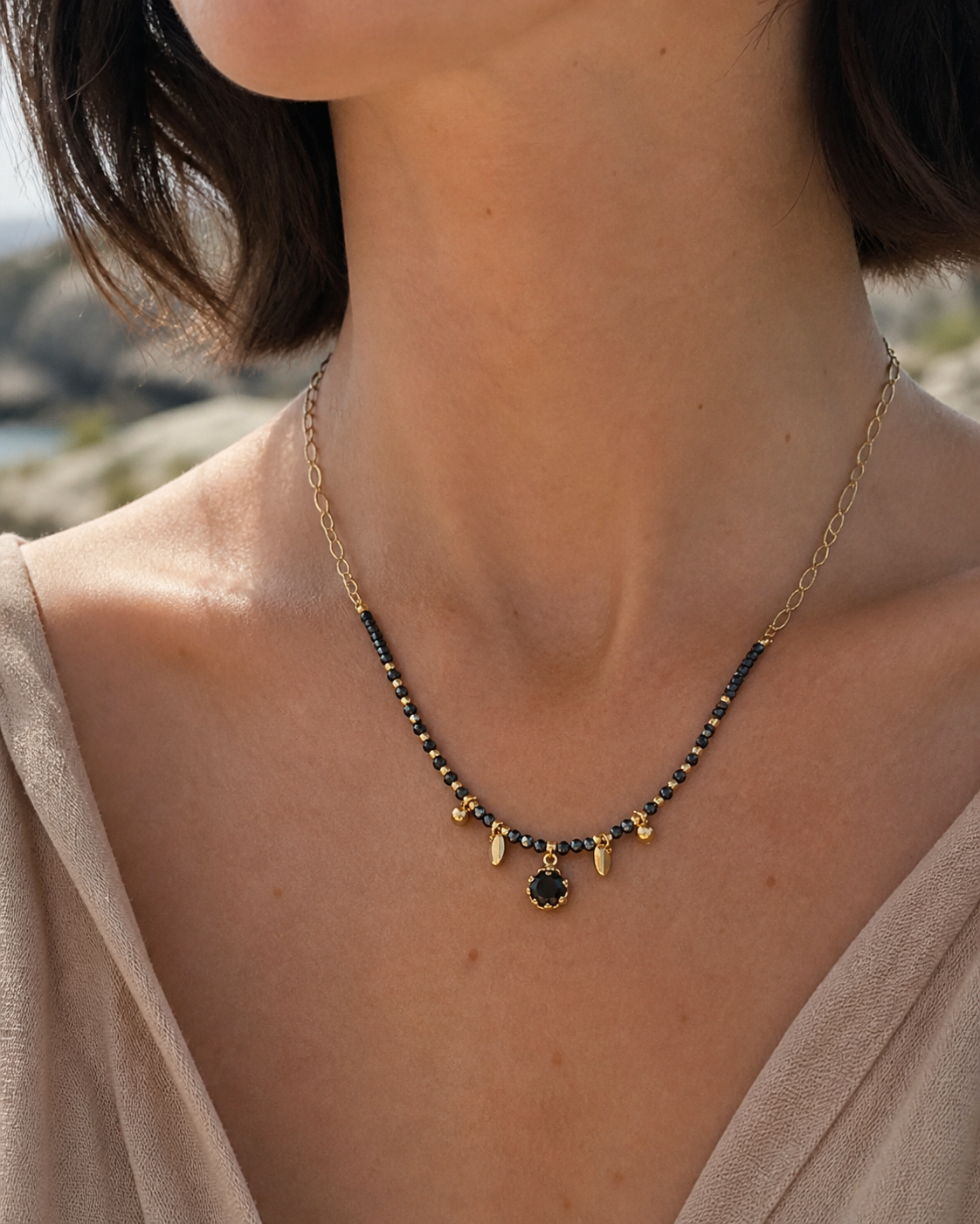 Collier doré Onyx porté au cou en lumière naturelle, pierres noires, strass central et chaîne acier inoxydable.
