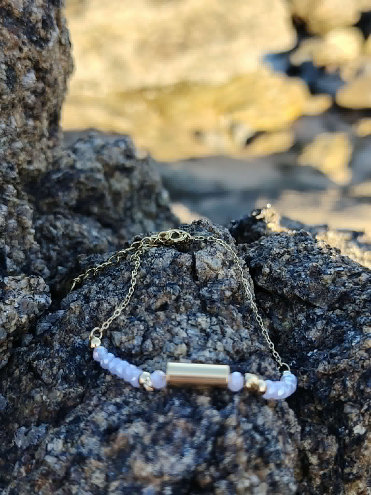 Bracelet Améthyste breloque longue posé sur rocher côtier, perles mauves et détails dorés pour clarté et douceur.