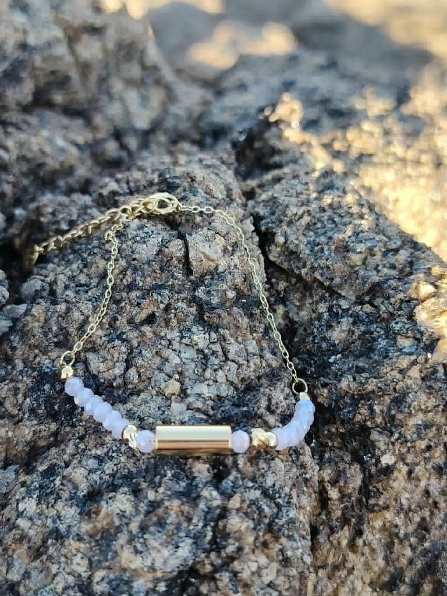 Bracelet Améthyste breloque dorée sur roche en bord de mer, perles lilas facettées et acier inoxydable pour sérénité.