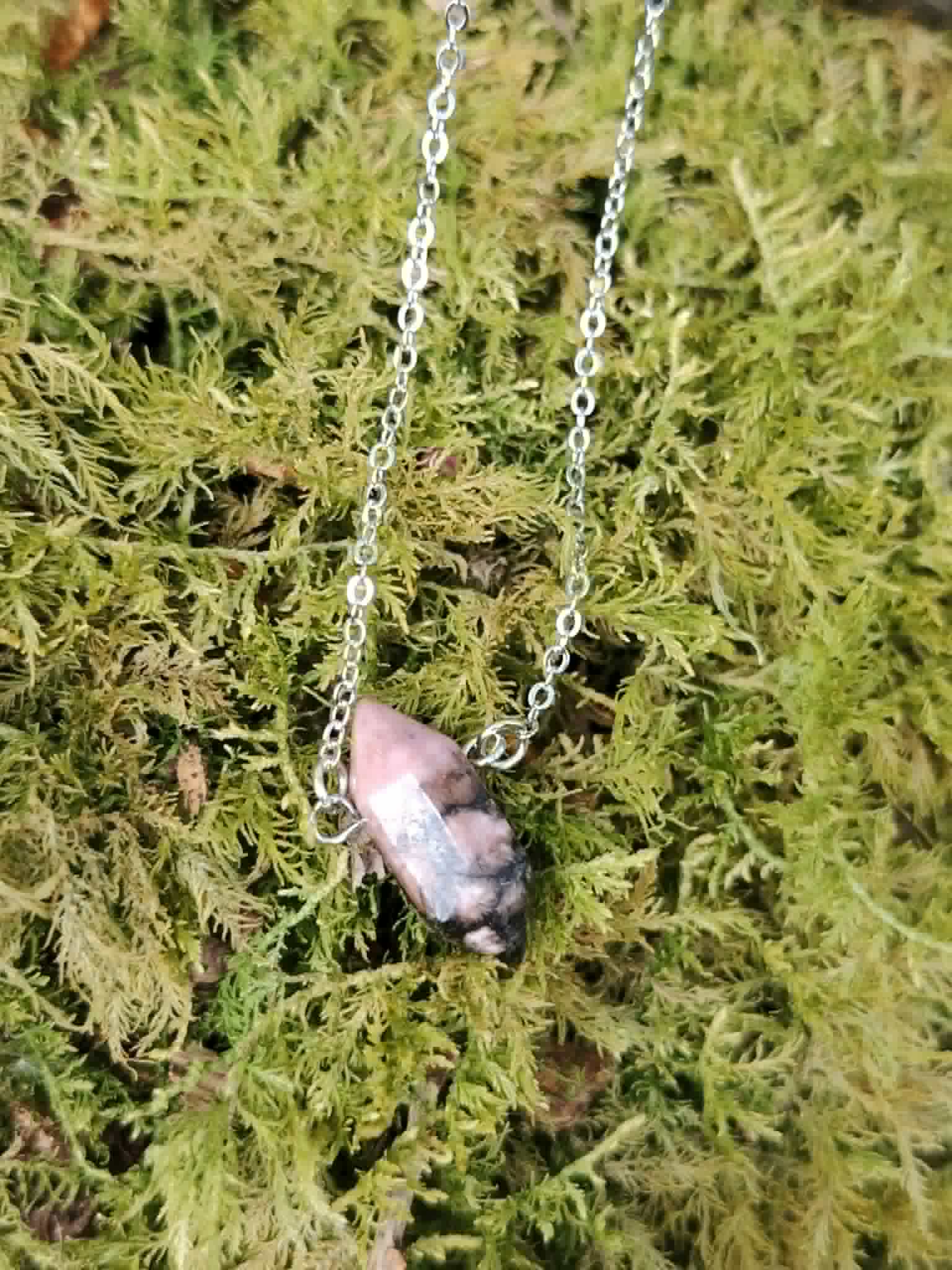 Pendentif Rhodonite naturelle en forme de pointe sur décor minéral, nuances roses et sombres pour équilibre intérieur.