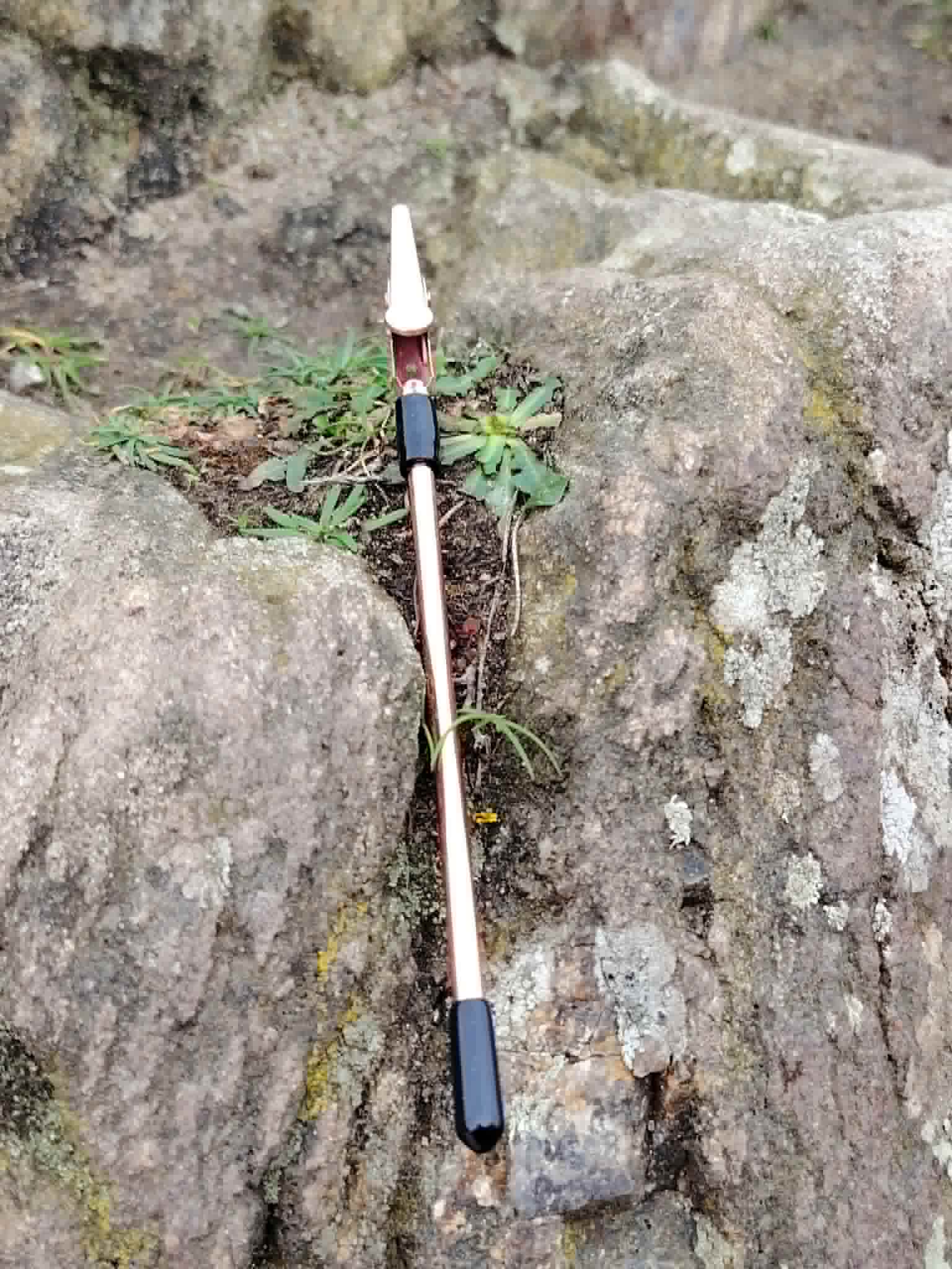 Outil aide fermoir pour bracelet présenté seul sur fond blanc, tige rose doré fine avec pince et embout noir.