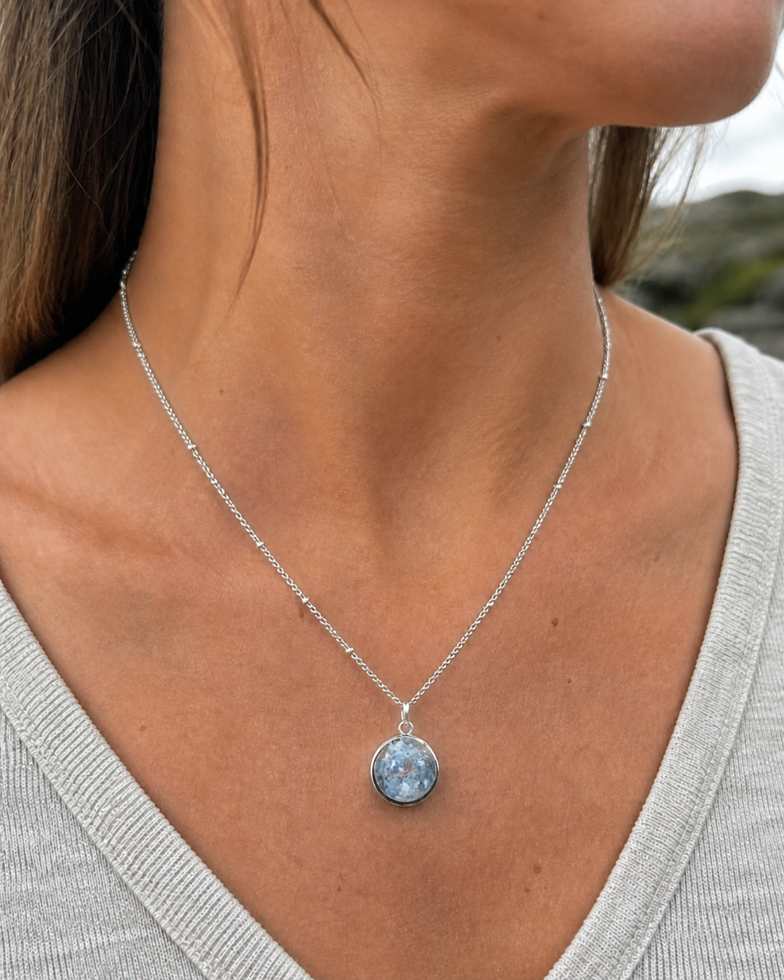 Collier Apatite en paillettes porté au cou, pendentif rond bleu argenté sur chaîne acier inoxydable avec haut gris clair.