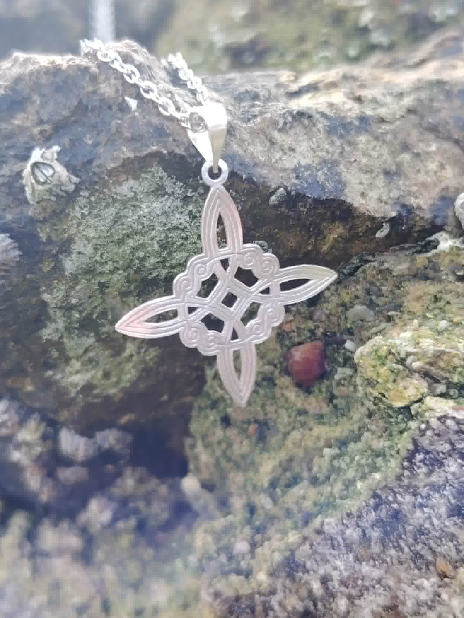 Pendentif Nœud de Sorcière en gros plan sur décor minéral, motif argenté ciselé pour une allure spirituelle.