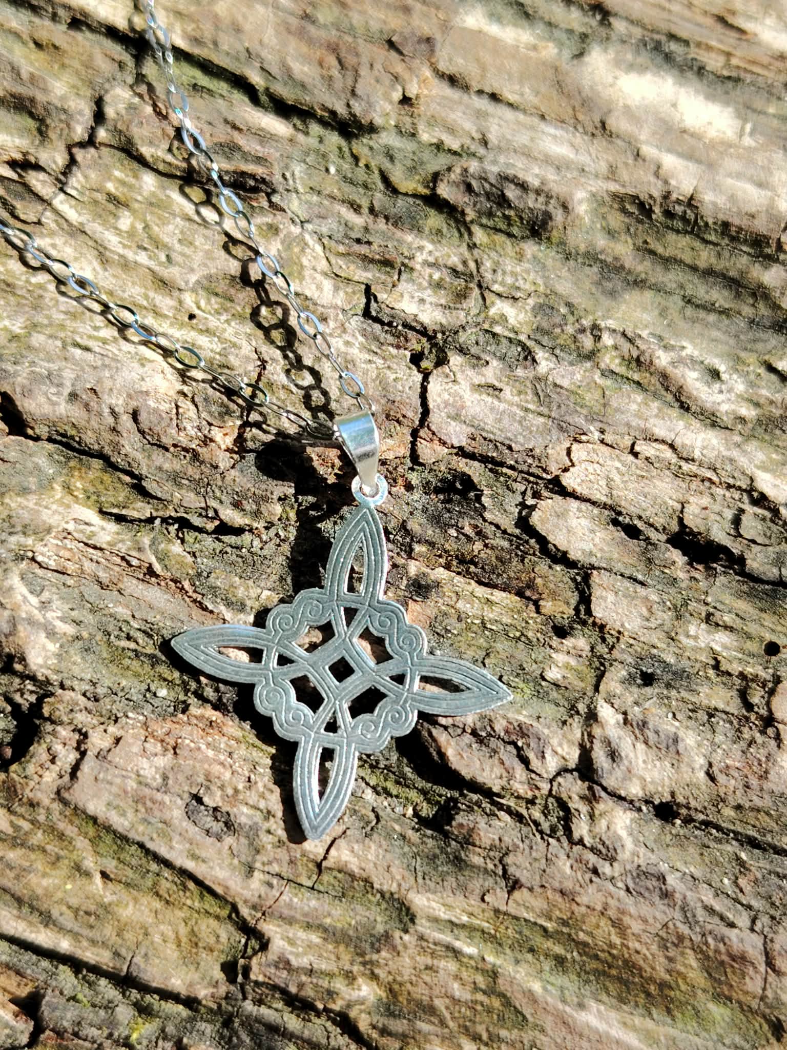 Pendentif Nœud de Sorcière en argent 925 posé sur écorce en lumière naturelle, bijou fin au motif entrelacé.
