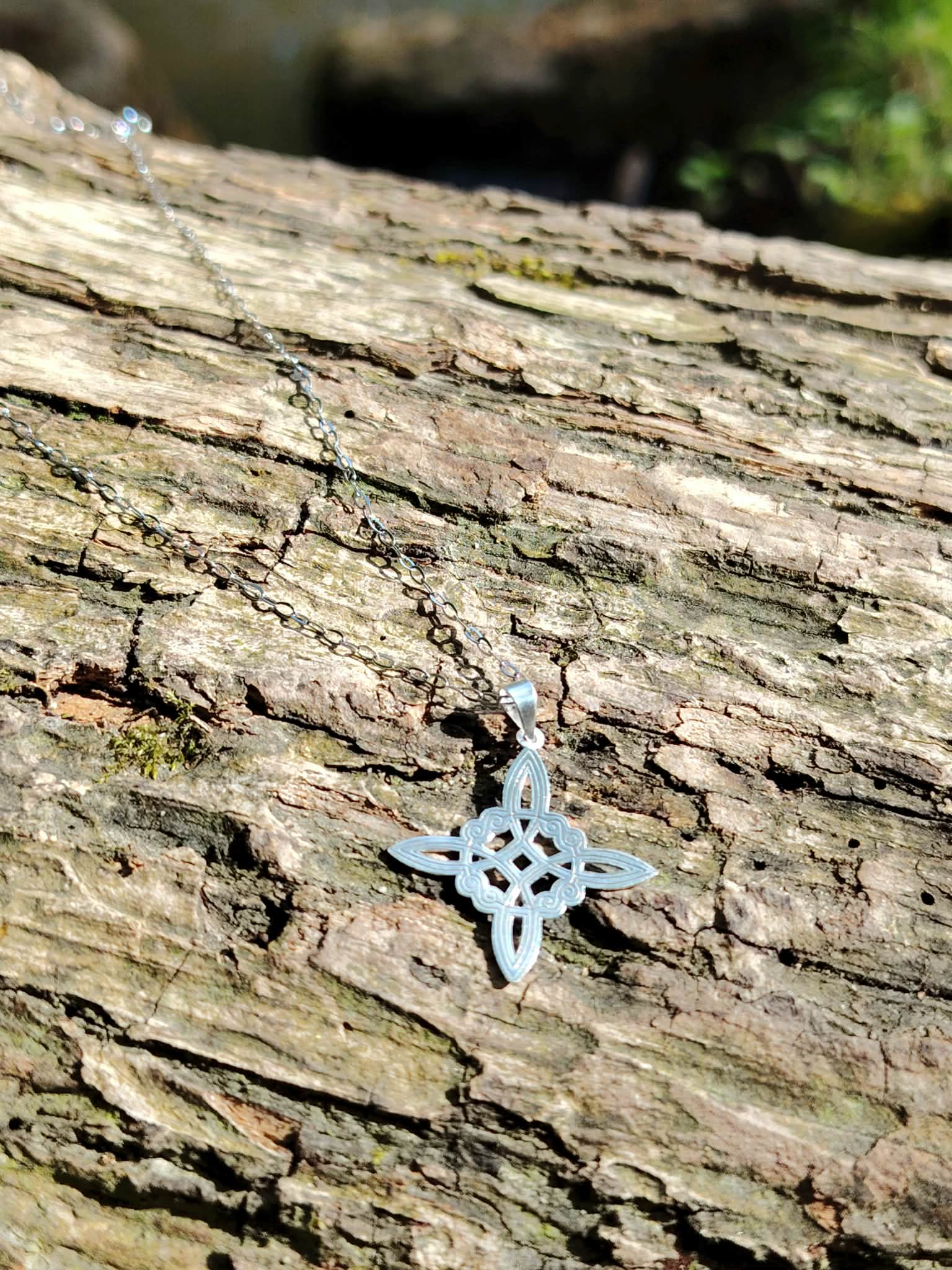 Pendentif Nœud de Sorcière fin posé sur tronc en extérieur, argent 925 lumineux avec chaîne argentée.