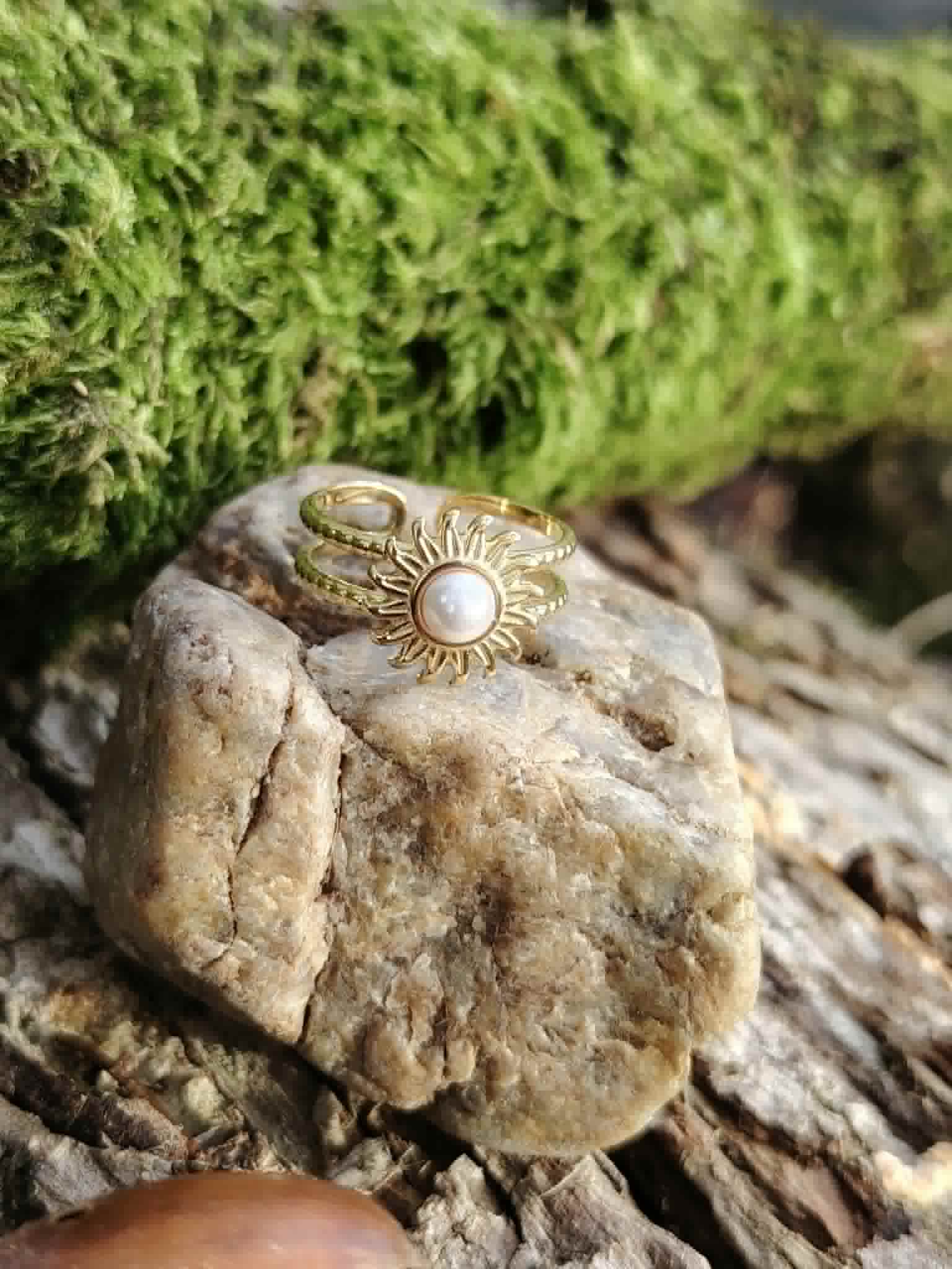 Bague motif Soleil sur pierre claire devant mousse verte, cabochon blanc nacré et double anneau doré ajustable.