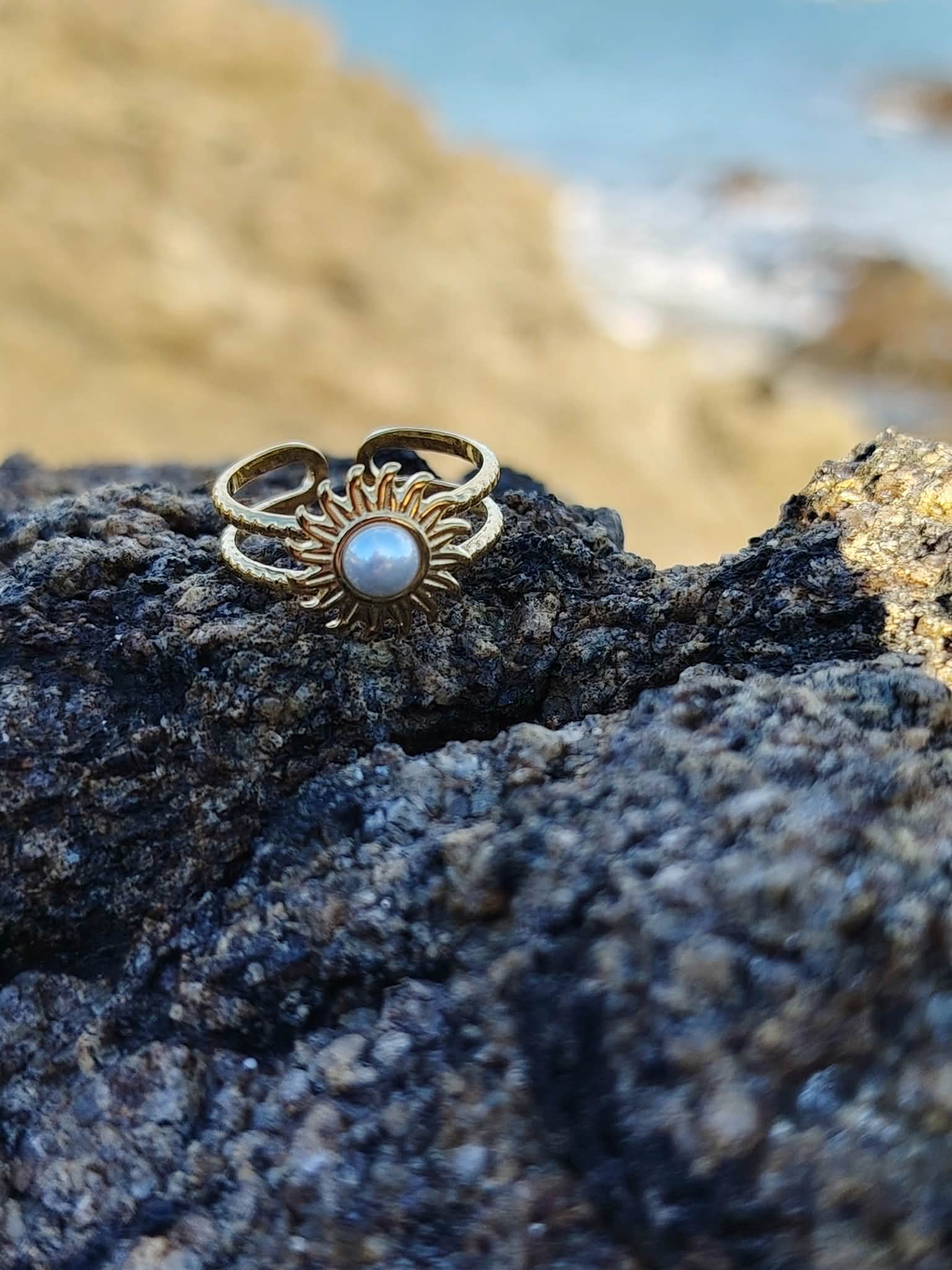 Bague ajustable cabochon nacré sur roche du bord de mer breton, motif solaire doré en lumière naturelle.