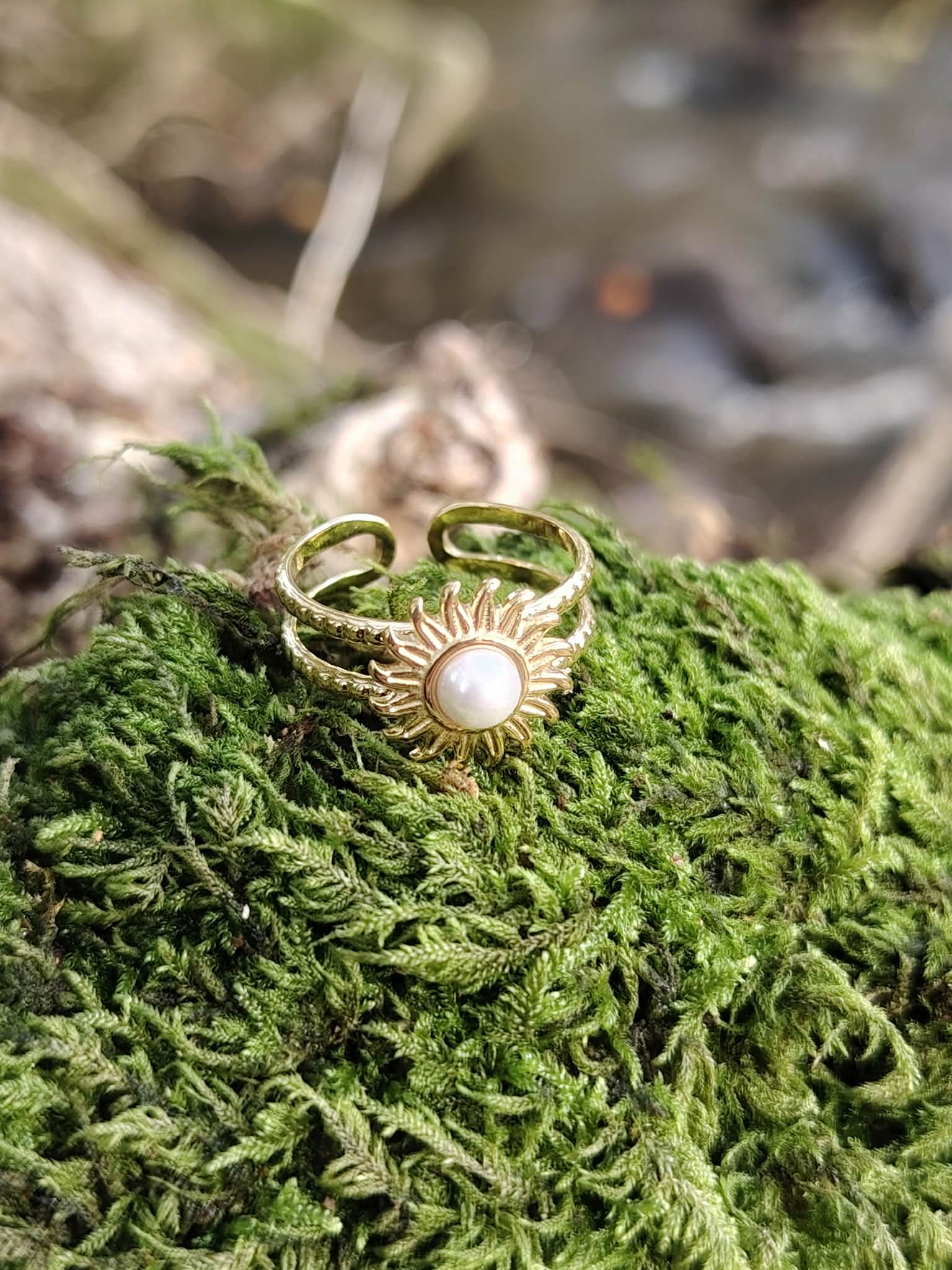 Bague dorée Soleil posée dans la mousse bretonne, anneau ajustable et cabochon blanc au style bohème lumineux.