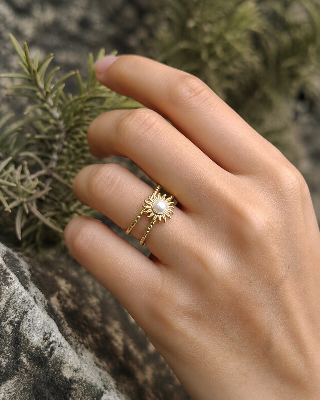 Bague Soleil portée au doigt en extérieur, motif rayonnant doré avec cabochon nacré pour une pose naturelle.