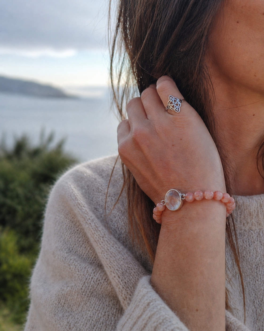 Bracelet en perles rose pâle avec cabochon central argenté porté en bord de mer en Bretagne, accompagné d’une bague nœud de sorcière pour douceur et protection.