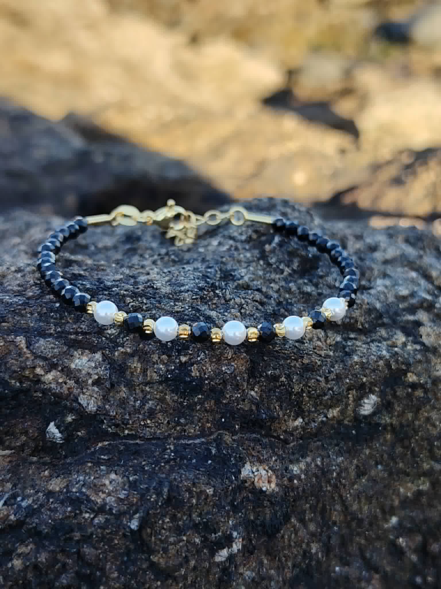 Bracelet Tourmaline Noire facettée 2 mm et cuivre plaqué or posé sur roche naturelle, bijou fin noir, blanc et doré pour ancrage et stabilité intérieure.
