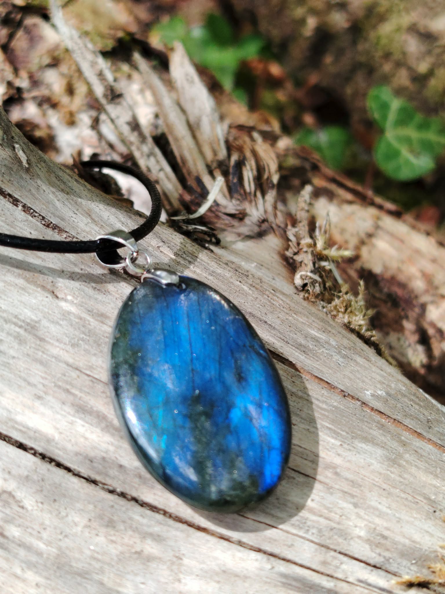 Gros plan sur pendentif Labradorite naturelle aux éclats bleu électrique, posé sur bois brut avec mousse, bijou minéral au charme mystérieux.