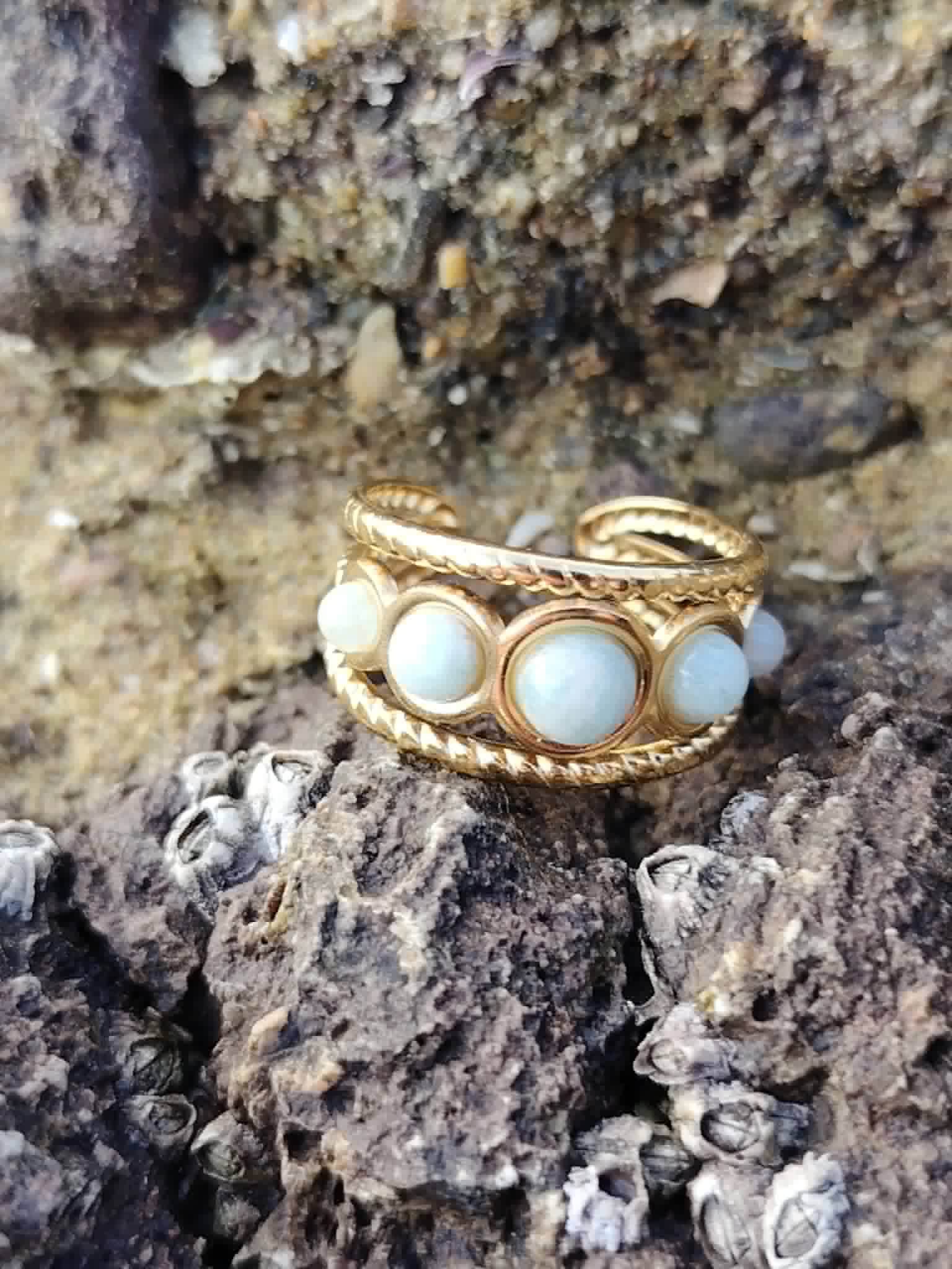 Gros plan sur bague réglable Amazonite dorée parmi roches et coquillages, pierres bleu-vert associées à la communication douce.