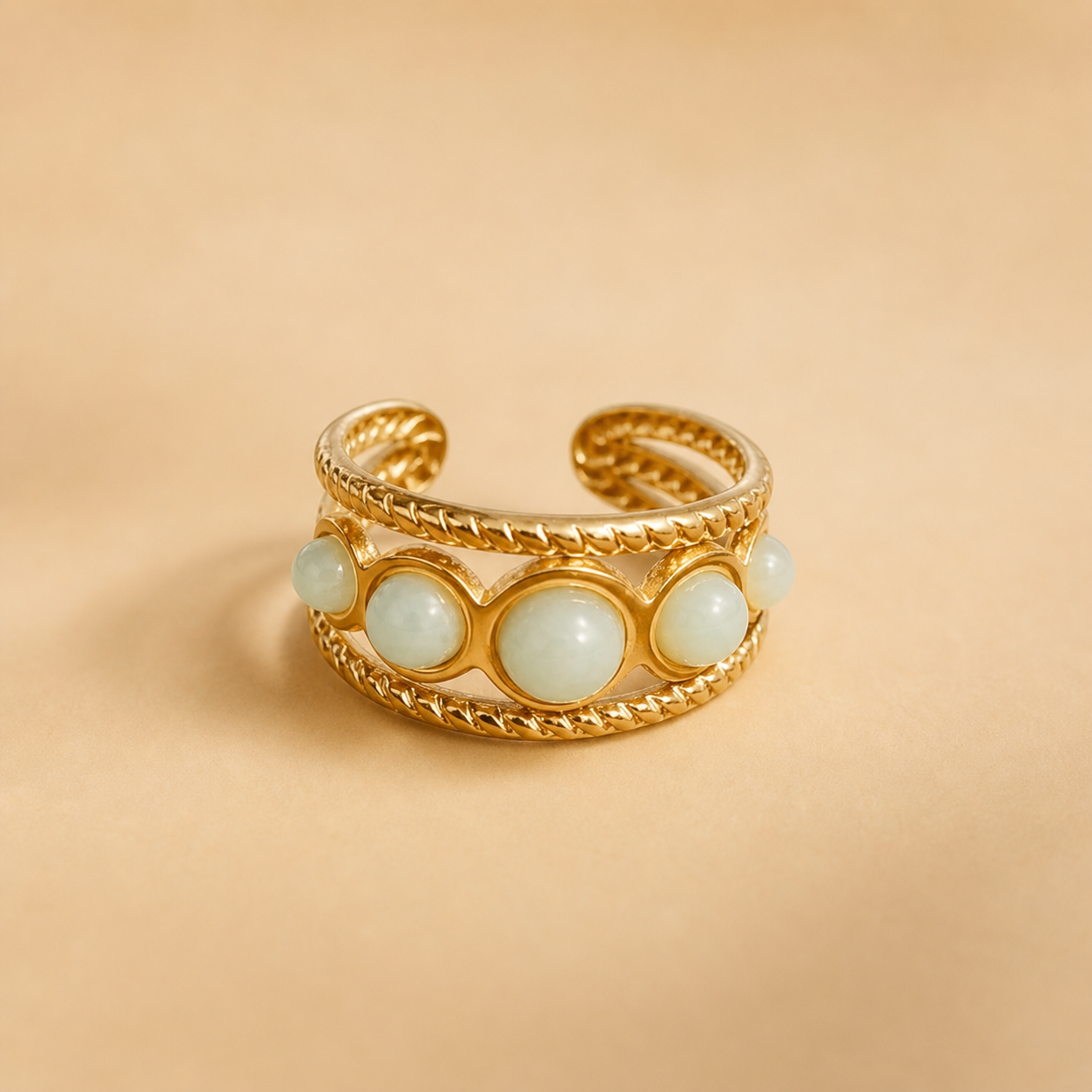 Bague dorée ajustable multi Amazonite sur fond beige doux, monture ajourée et cabochons bleu-vert pour équilibre émotionnel.
