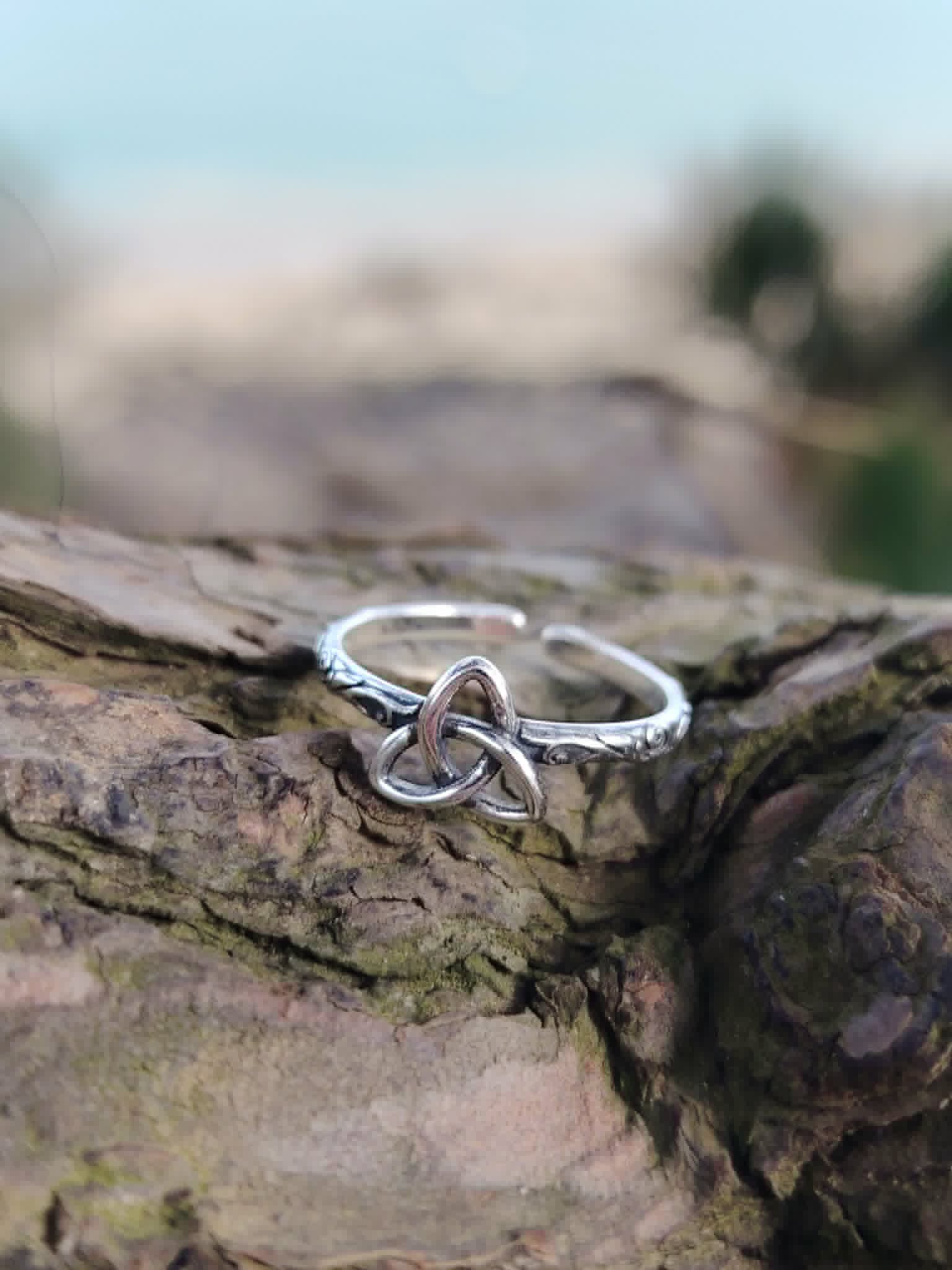 Bague Triquetra Argent 925 ajustable posée sur bois naturel, symbole celtique argenté avec arrière-plan marin flou pour harmonie et protection.