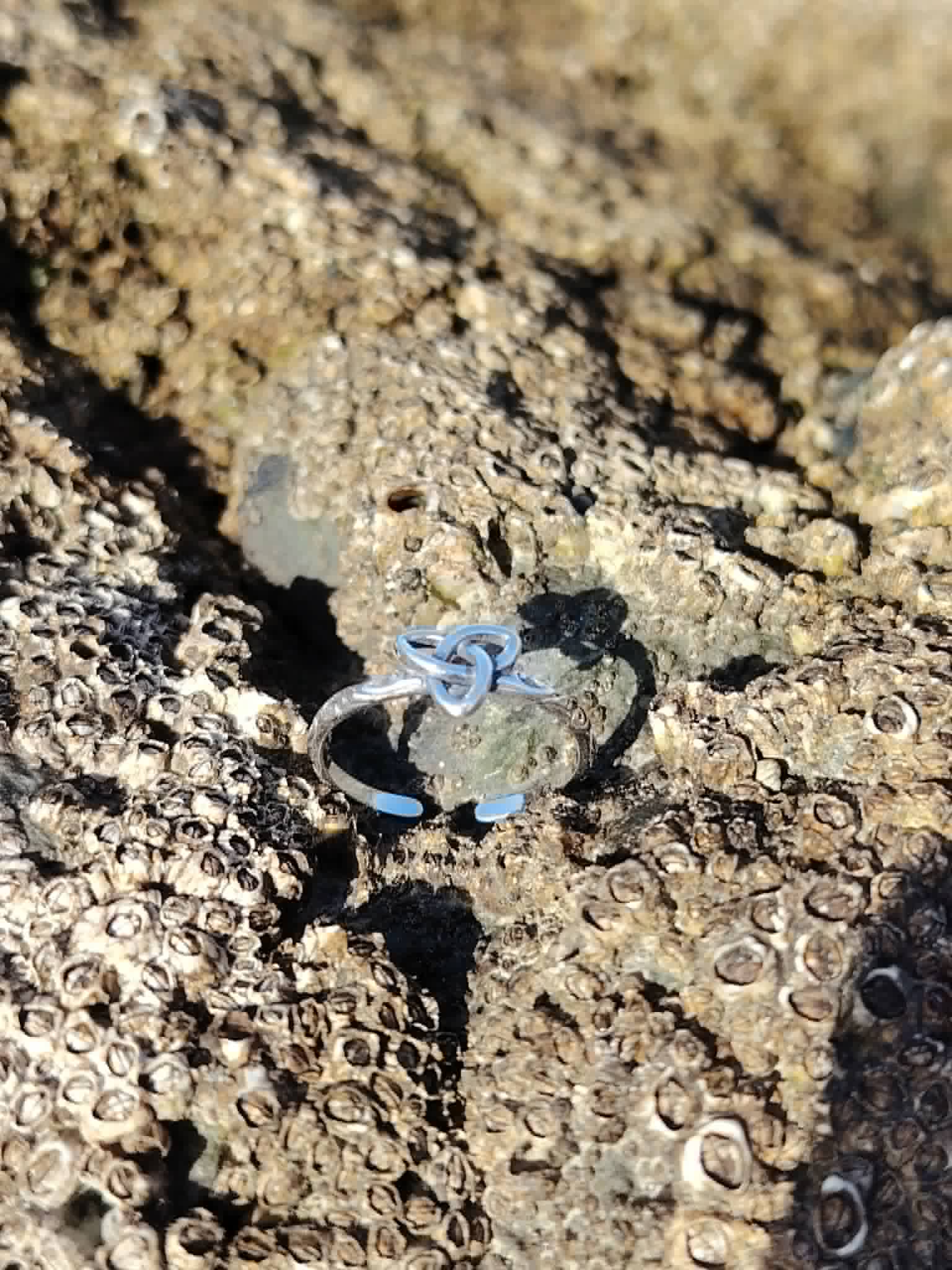 Bague Triquetra argentée vue de dessus sur roche naturelle coquillée, anneau ouvert et symbole celtique pour équilibre et intention.