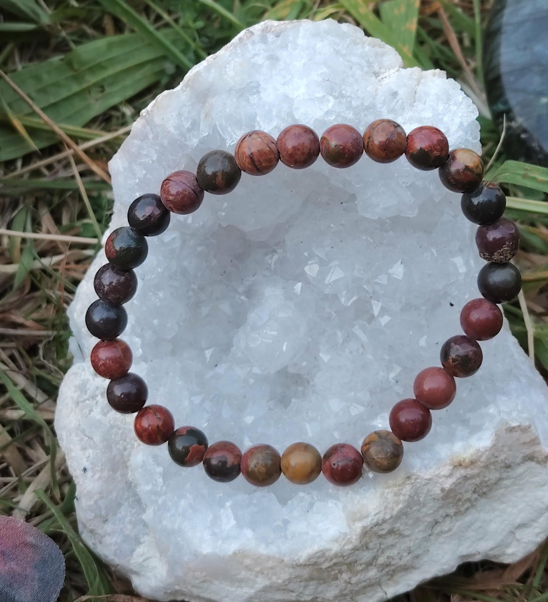 Bracelet Jaspe Polychrome posé sur une druse blanche en extérieur, perles multicolores aux nuances terre et feu, pour protection et stabilité émotionnelle.