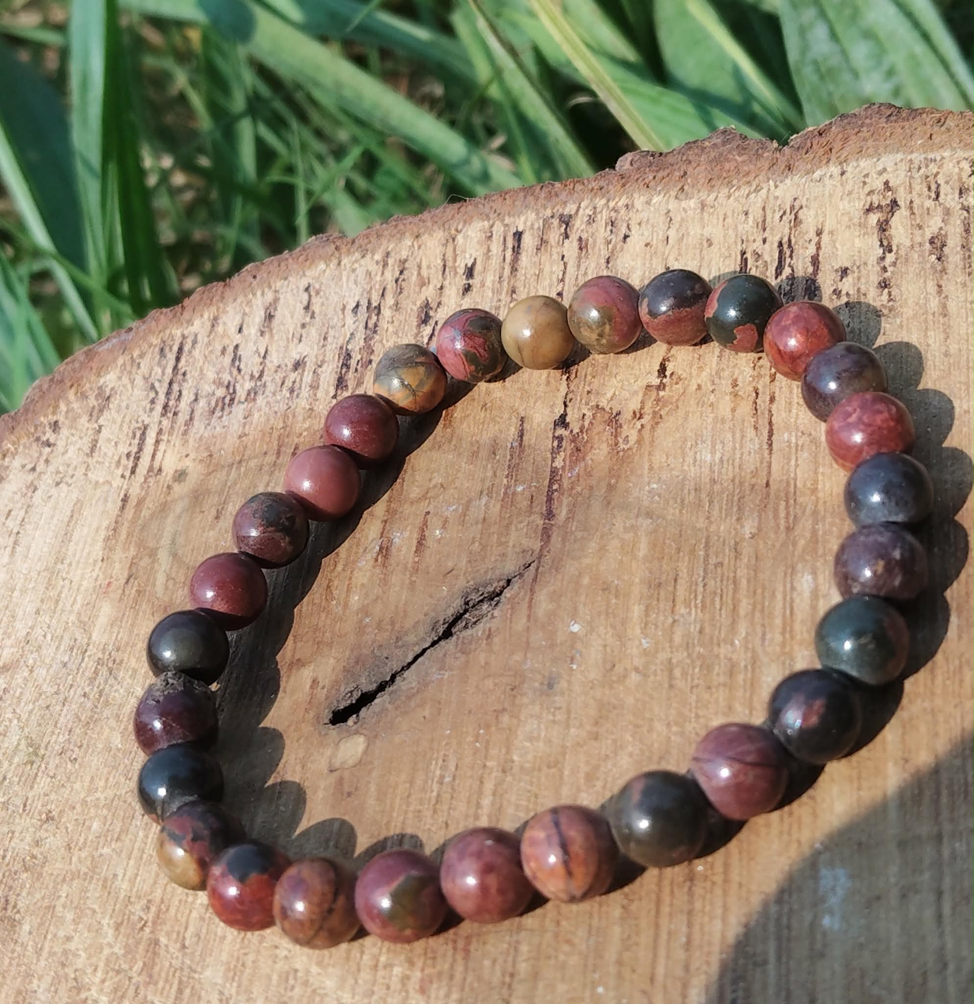 Bracelet Jaspe Polychrome posé sur une tranche de bois en extérieur, perles aux teintes bordeaux, ocre et sombres, pour force tranquille et ancrage.