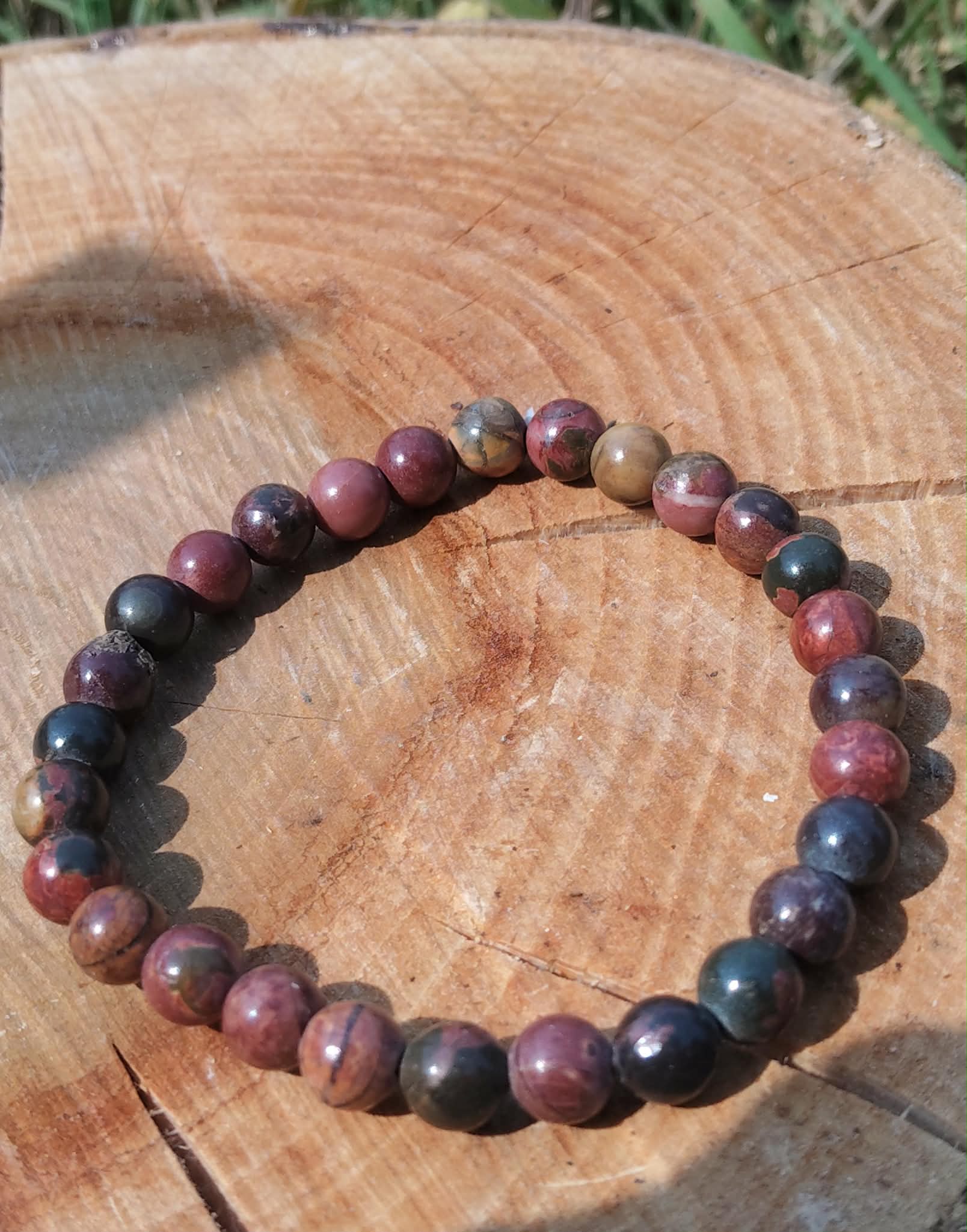 Bracelet Jaspe Polychrome sur rondin de bois au soleil, perles naturelles rouge brun, beige et noir, pour présence, courage et enracinement.