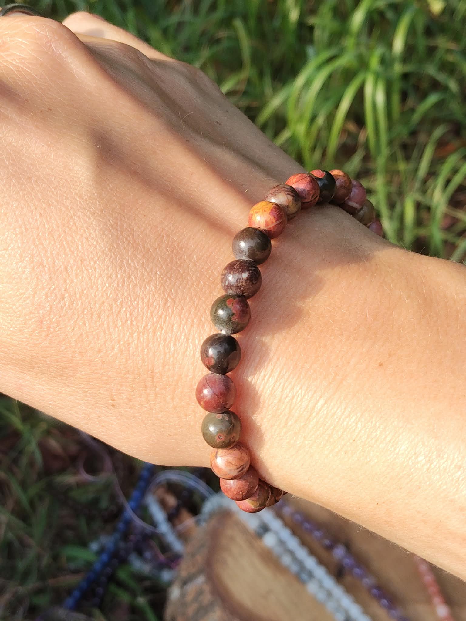Bracelet Jaspe Polychrome porté au poignet en lumière naturelle, perles aux tons terreux et marbrés sur fond végétal, pour sérénité et confiance en soi.