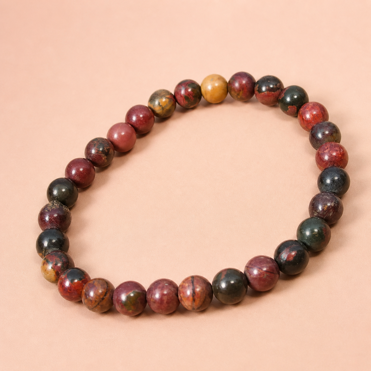 Bracelet Jaspe Polychrome en perles rondes sur fond beige rosé, nuances terreuses rouge brun, ocre et noir, pour stabilité intérieure et recentrage.