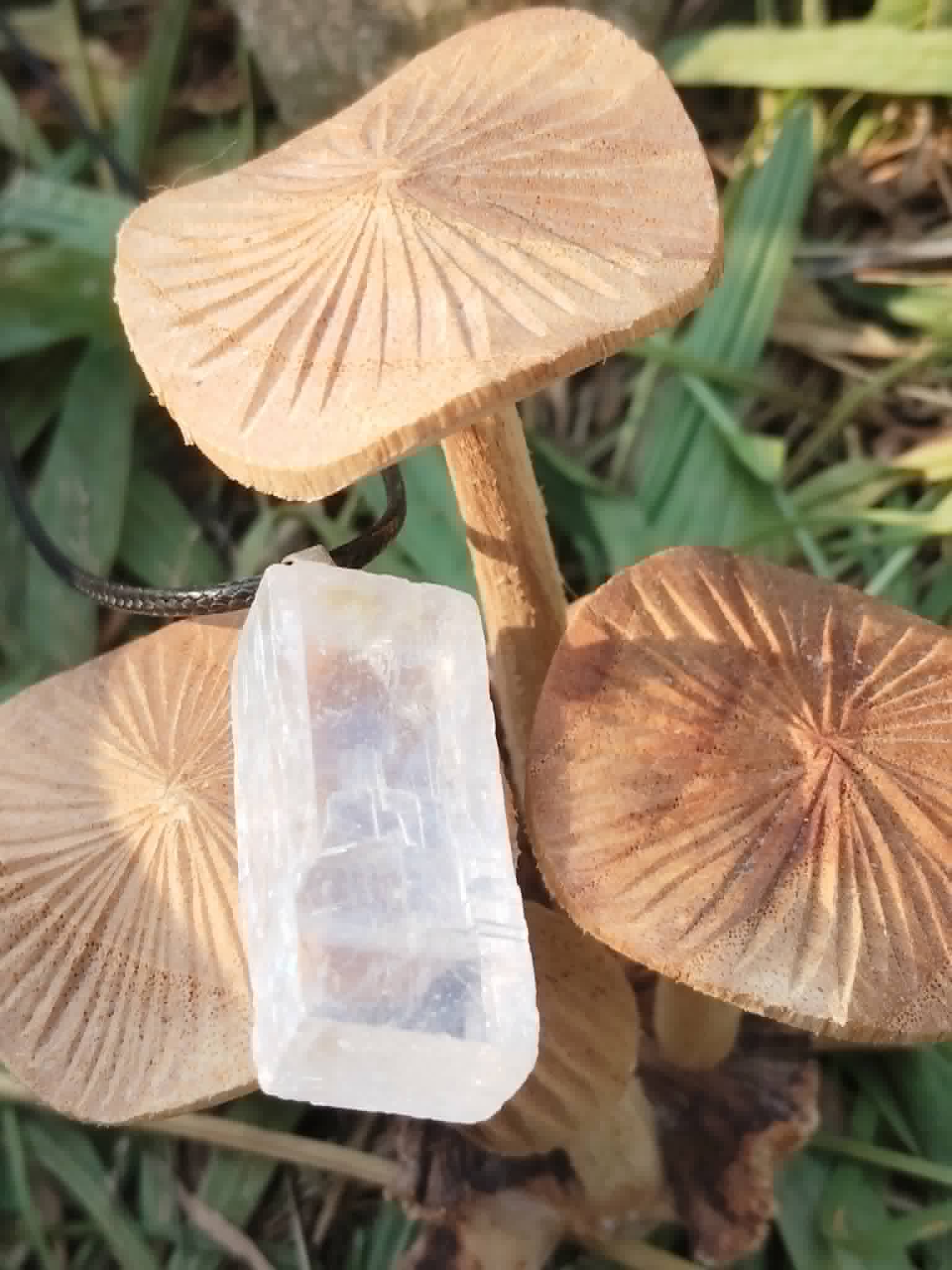 Pendentif Calcite Optique présenté entre champignons décoratifs en bois, pierre claire et cordon noir pour douceur mentale et énergie cristalline.