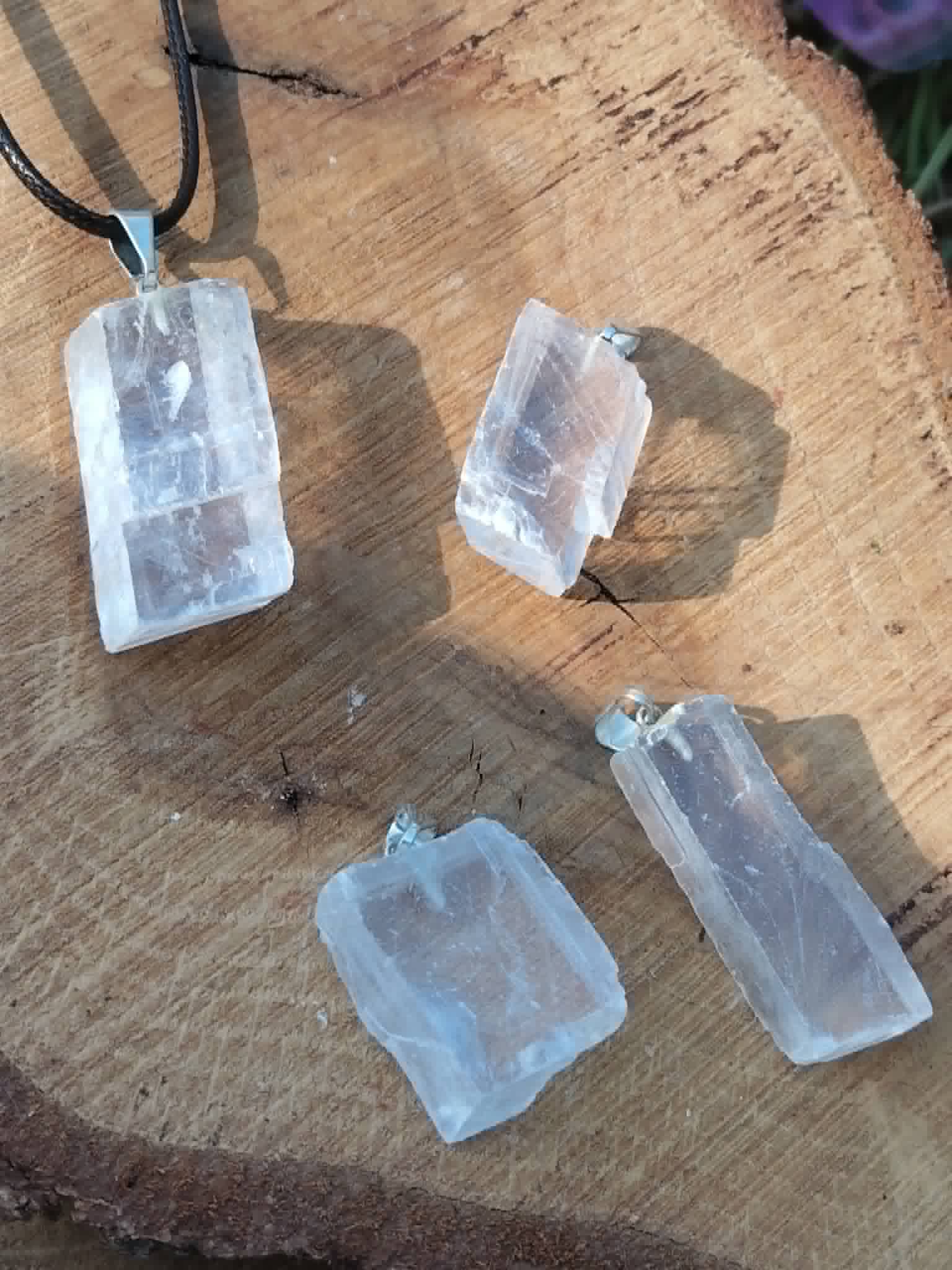 Quatre pendentifs Calcite Optique sur tranche de bois, formes brutes transparentes avec bélières argentées pour recul et vision intérieure.
