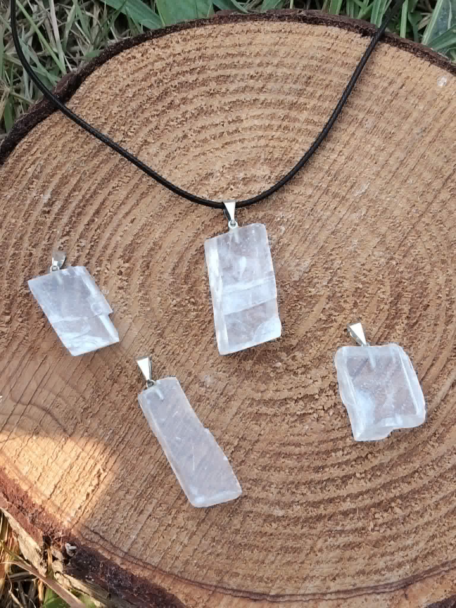 Plusieurs pendentifs en Calcite Optique sur rondin de bois et herbes, pierres transparentes aux formes variées pour méditation et lumière intérieure.