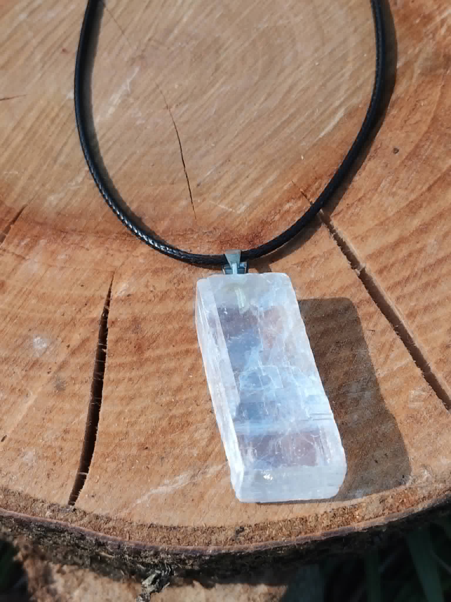 Pendentif Calcite Optique sur rondin de bois fendu, pierre claire rectangulaire avec cordon noir pour discernement et recentrage.