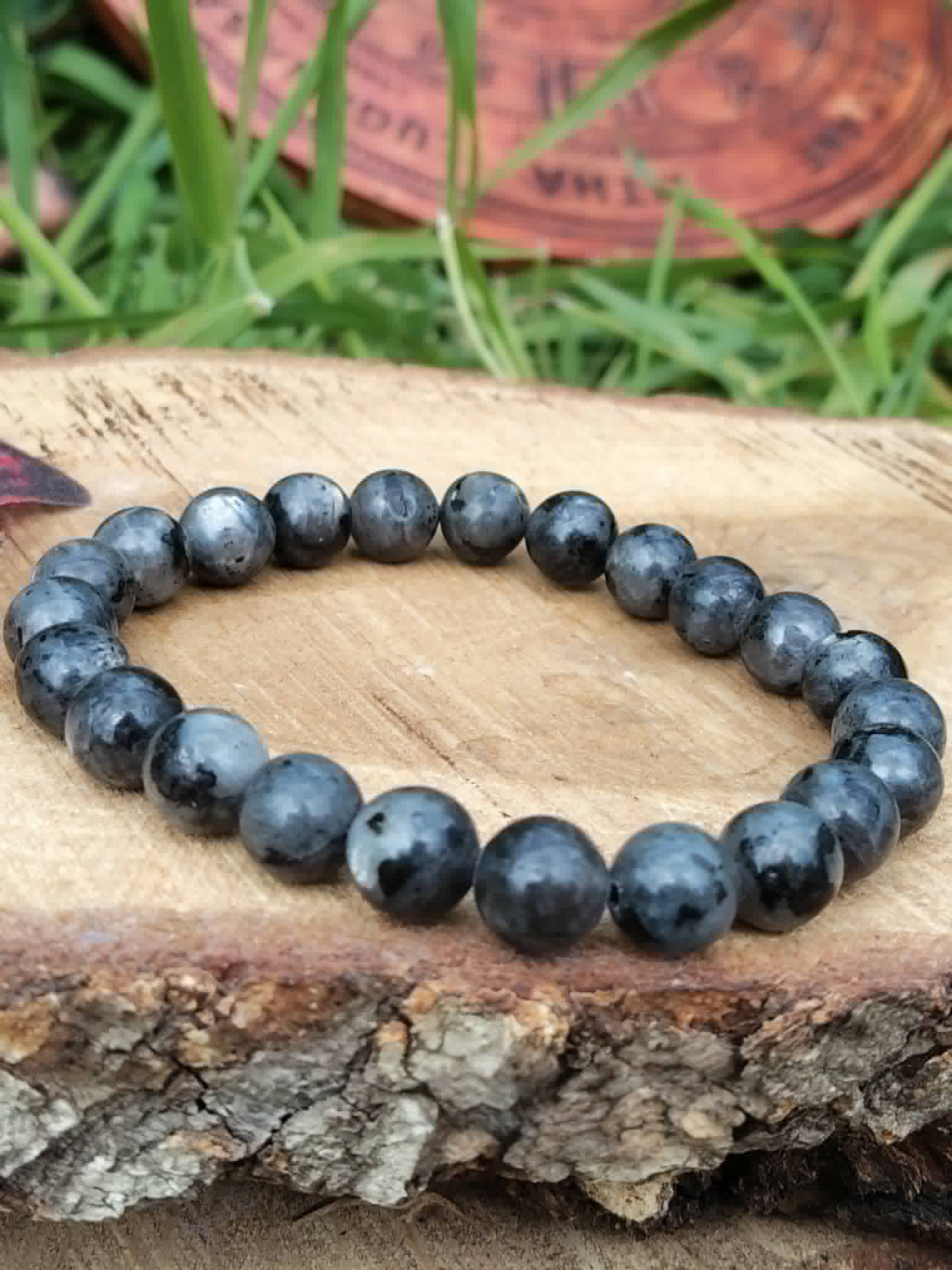 Bracelet Larvikite 8 mm posé sur tranche de bois en extérieur, perles gris charbon, concentration et recul intérieur.