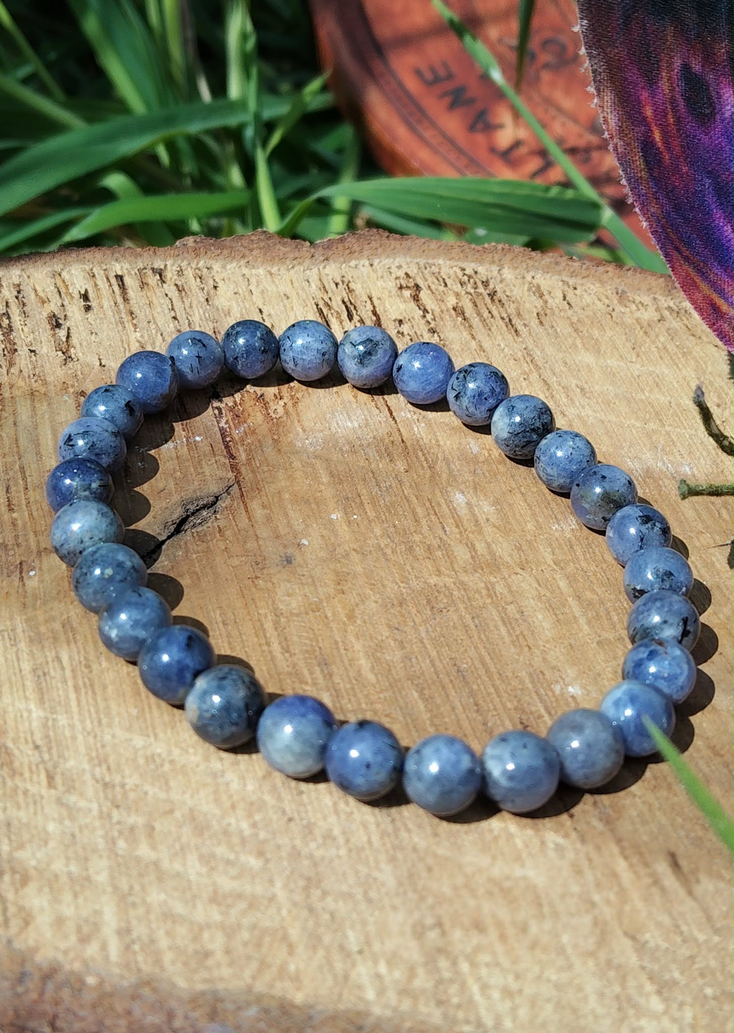 Bracelet Tanzanite 6-7 mm sur tranche de bois avec herbe, bijou en perles naturelles pour confiance en soi et créativité.