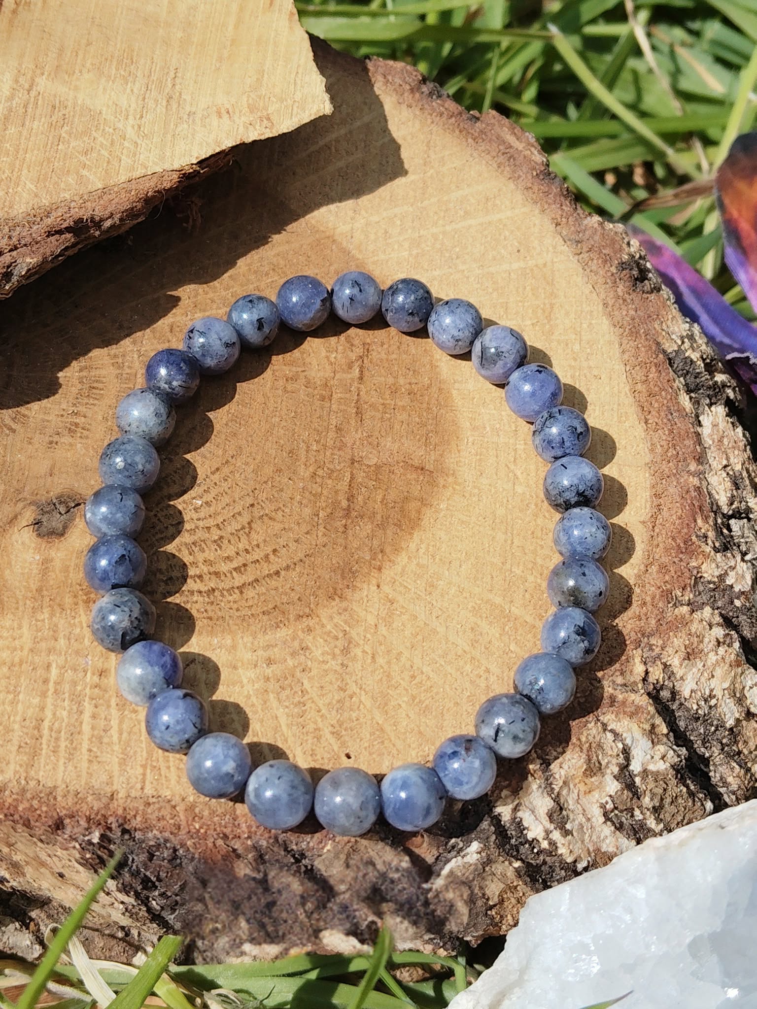 Bracelet Tanzanite 6 à 7 mm sur rondin de bois au soleil, perles bleu lavande pour intuition et transformation spirituelle.