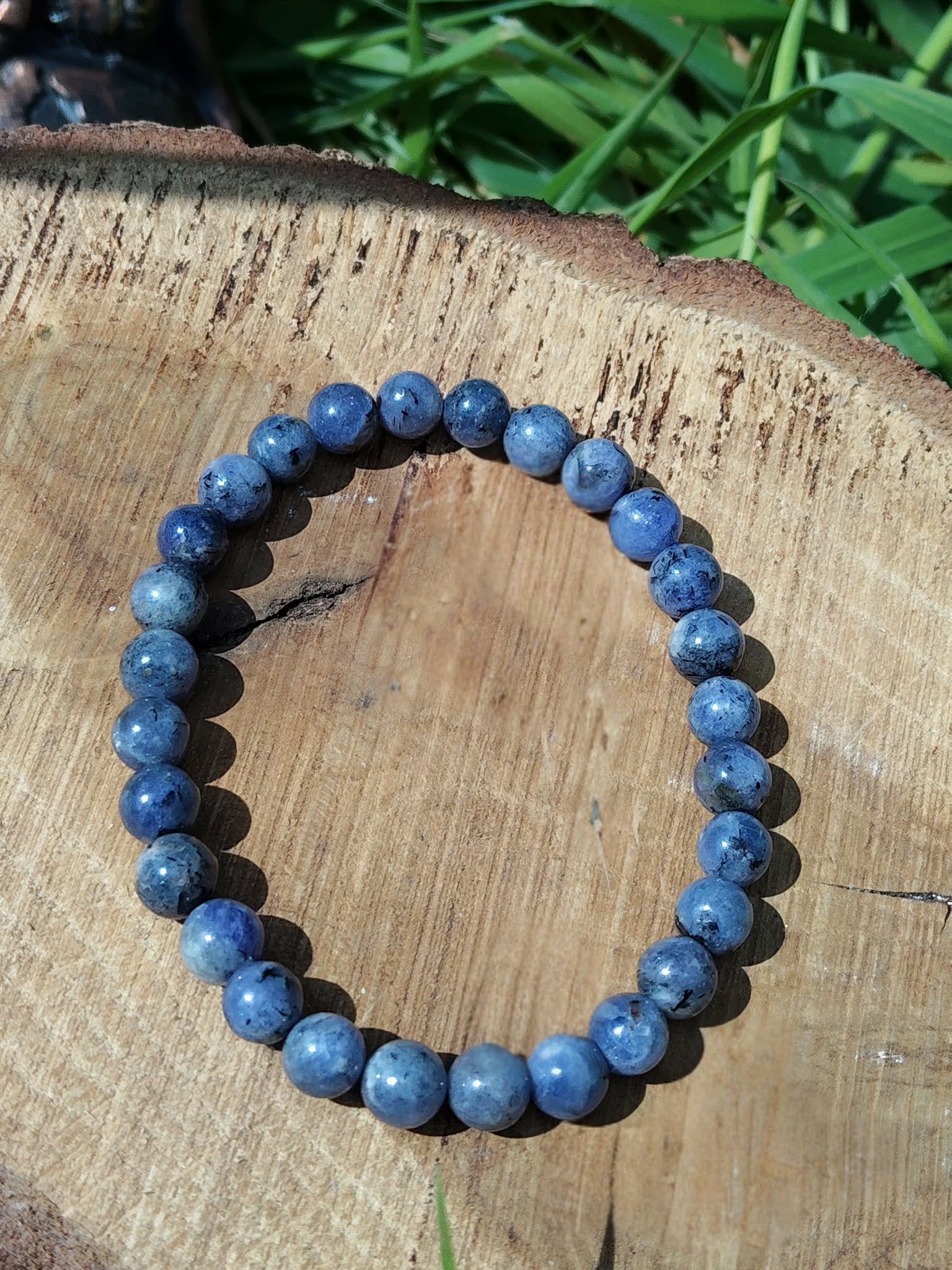 Bracelet Tanzanite naturelle posé sur bois clair en extérieur, perles bleutées pour clarté mentale et communication authentique.