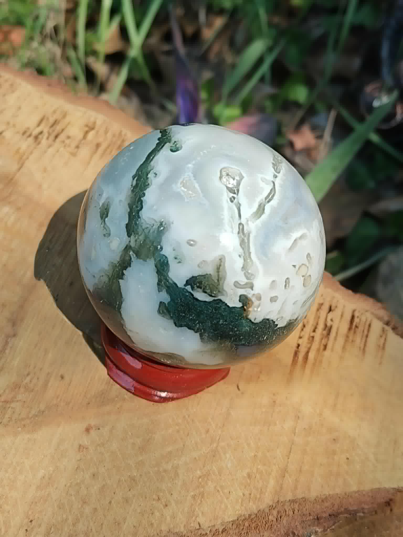 Sphère Agate Arbre sur tranche de bois en extérieur, pierre blanche et vert mousse associée à l’ancrage doux.