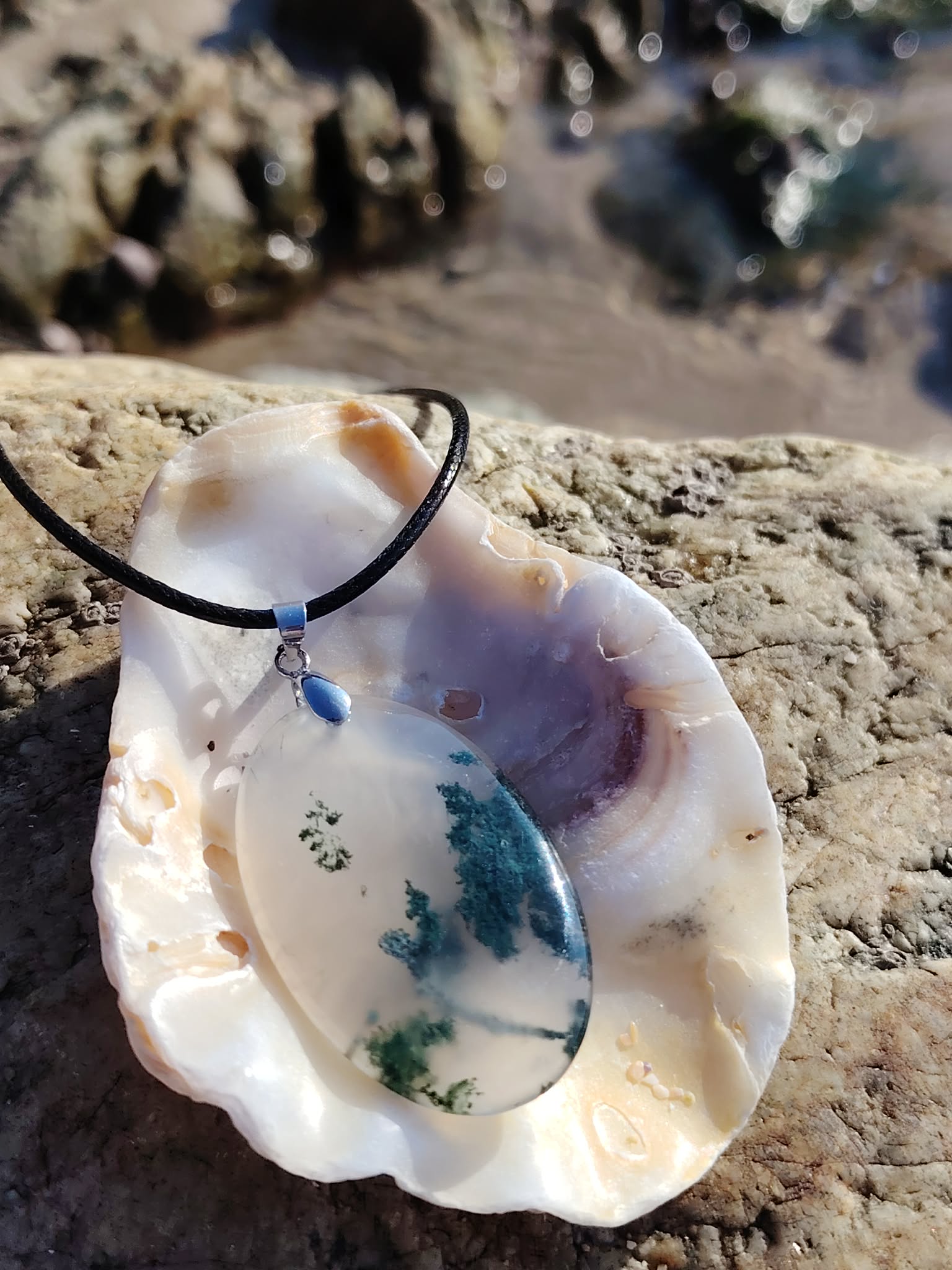 Collier Agate Mousse présenté sur coquillage au bord de l’eau en Bretagne, bijou lié à l’ancrage doux.