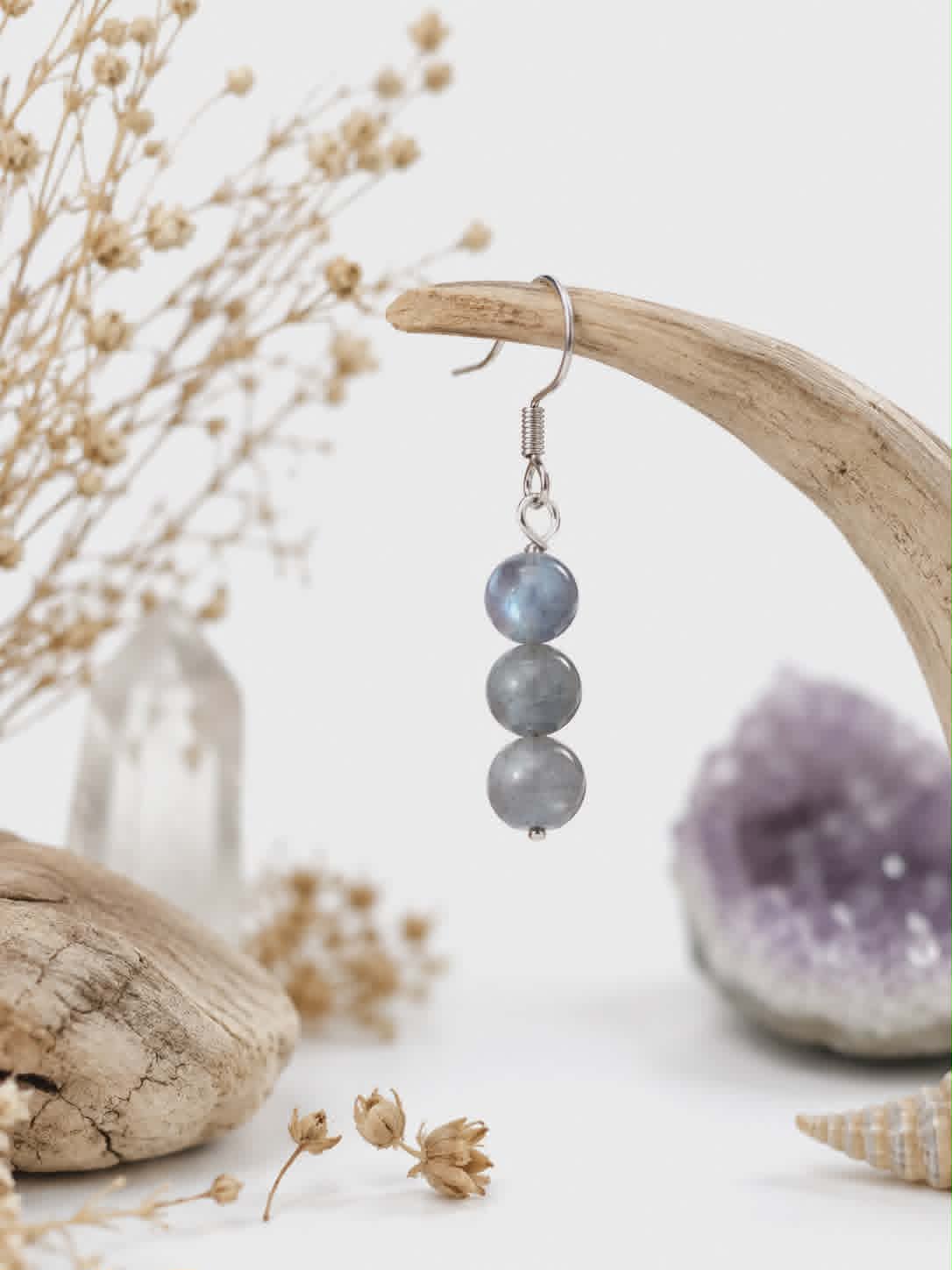 Boucle d’oreille Labradorite Magic Gaïa suspendue sur bois flotté, fleurs séchées, améthyste floue et clarté.