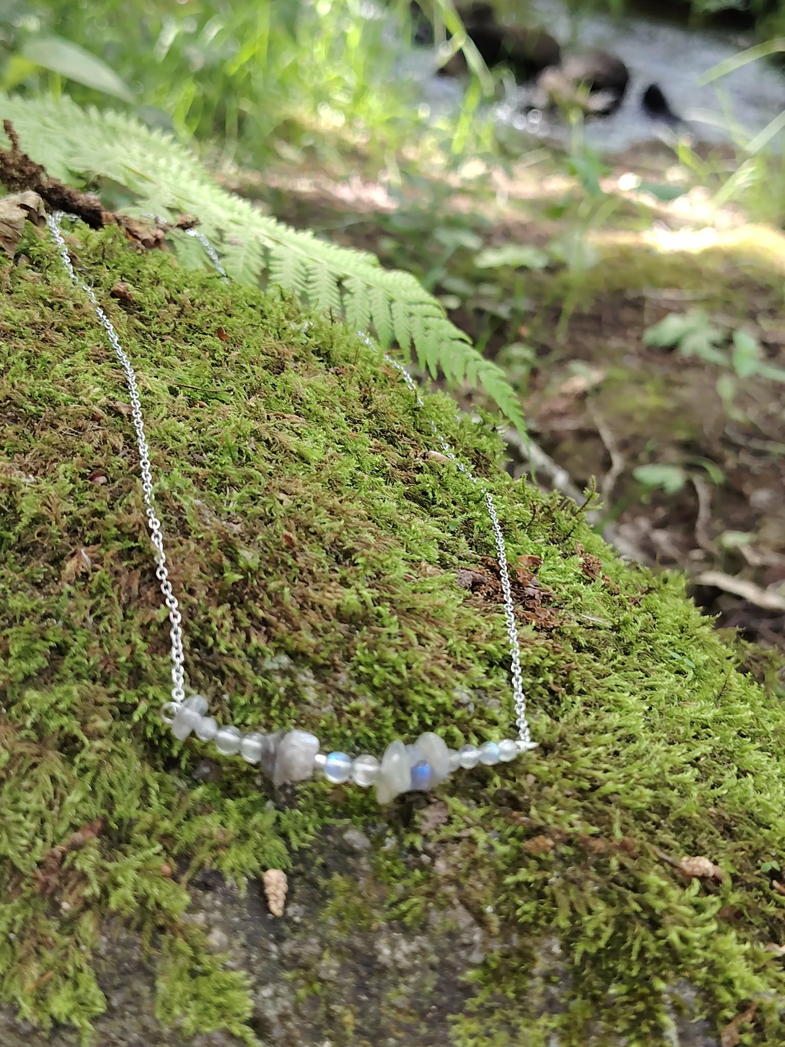 Bijou Labradorite en décor forestier, chaîne argentée délicate et pierres grises associées à la protection énergétique.